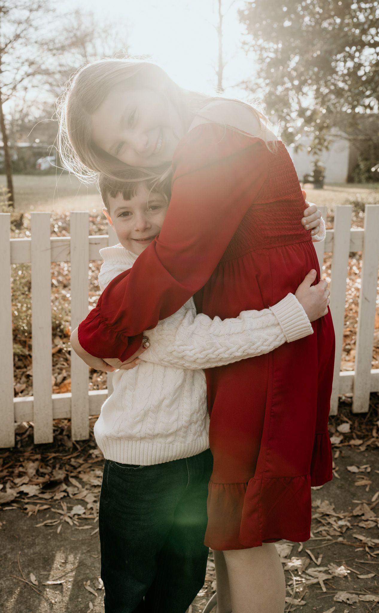 A heartwarming autumn scene shows two people in red and white sweaters embracing by a white picket fence.