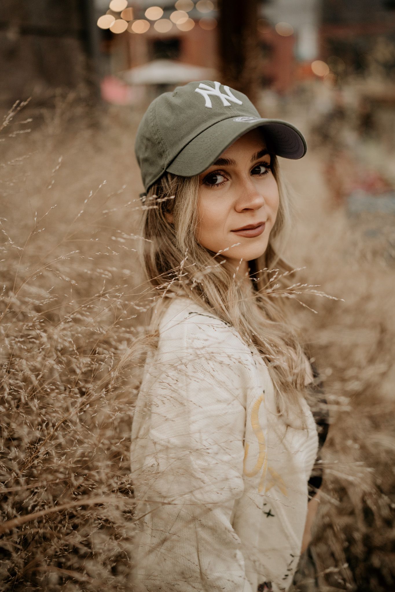 A series of outdoor portraits showing someone wearing a NY Yankees cap and white sweater against a natural brown backdrop.
