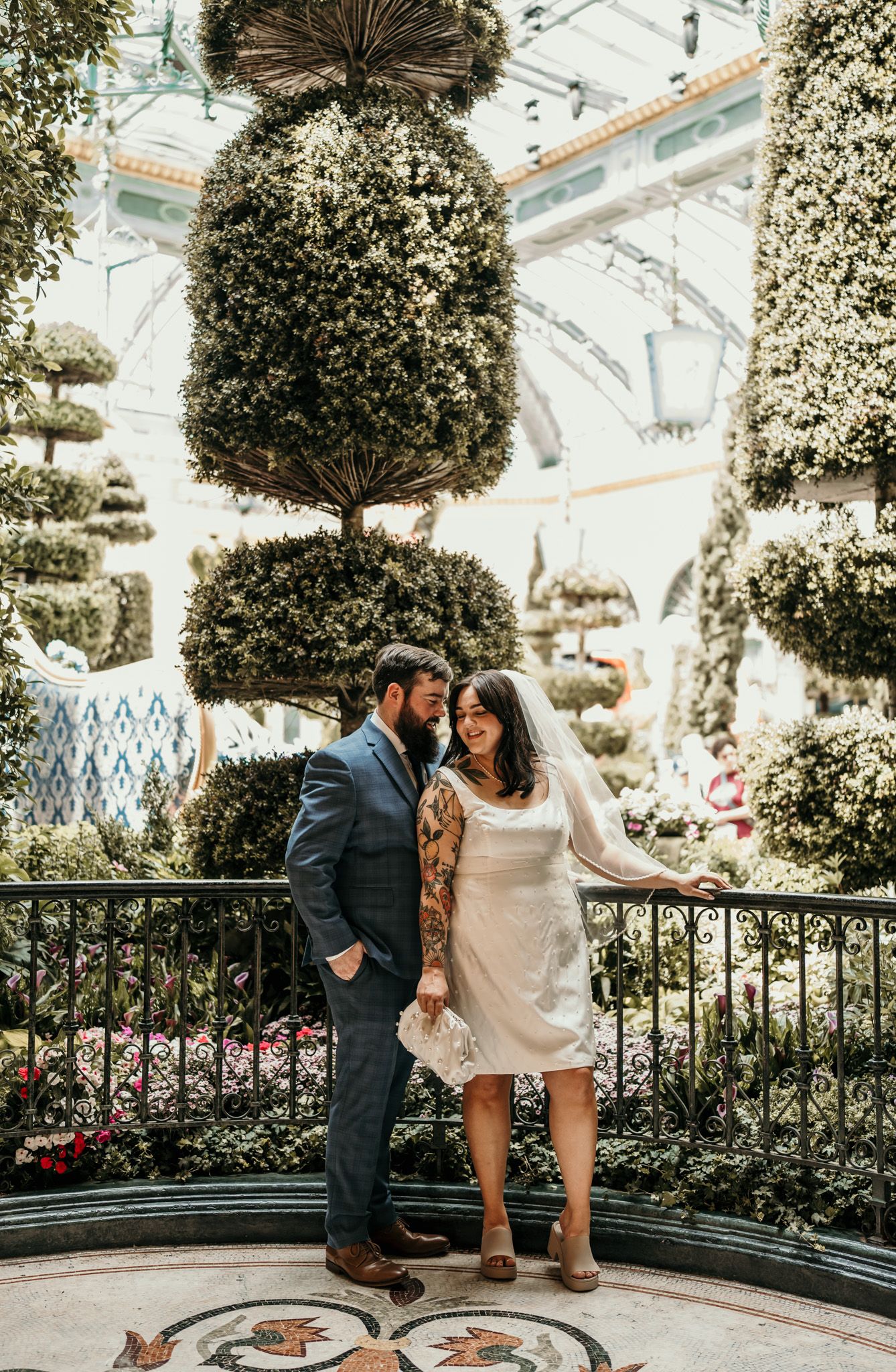 Couple shares romantic moments in a conservatory garden with hanging plants and decorative railing.