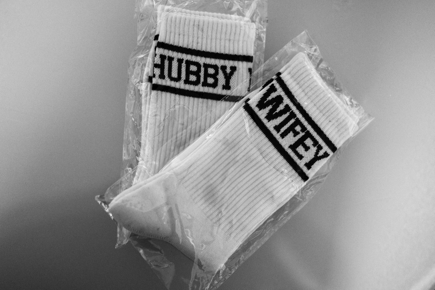 Black and white photograph showing two pairs of socks. One that says hubby and the other that says wifey.