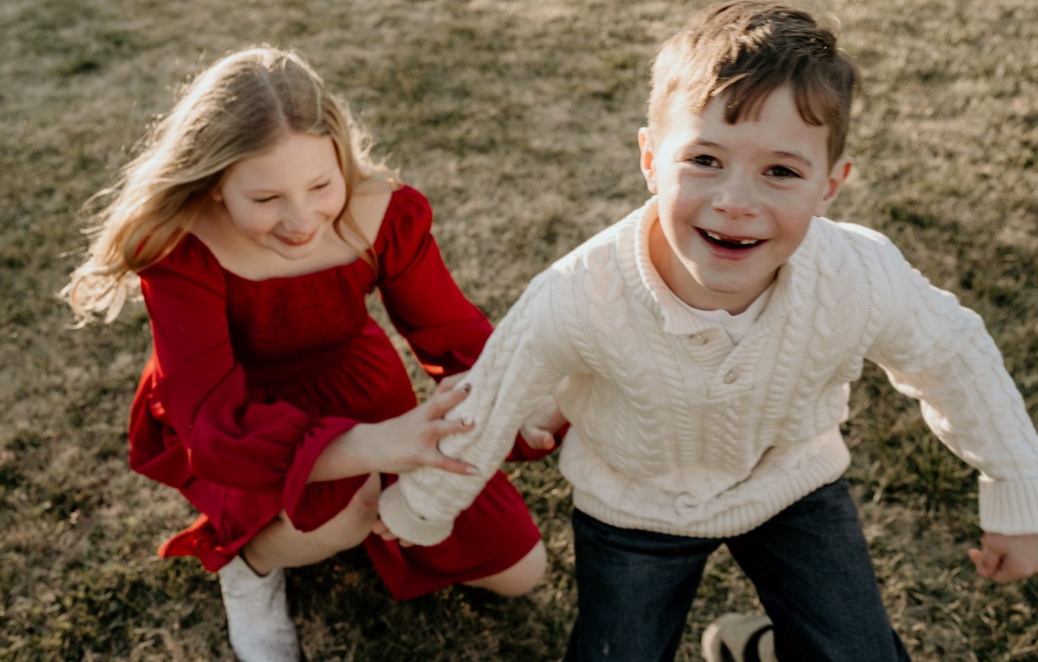 Two children in winter outfits hold hands while playing and laughing together outdoors in natural lighting.