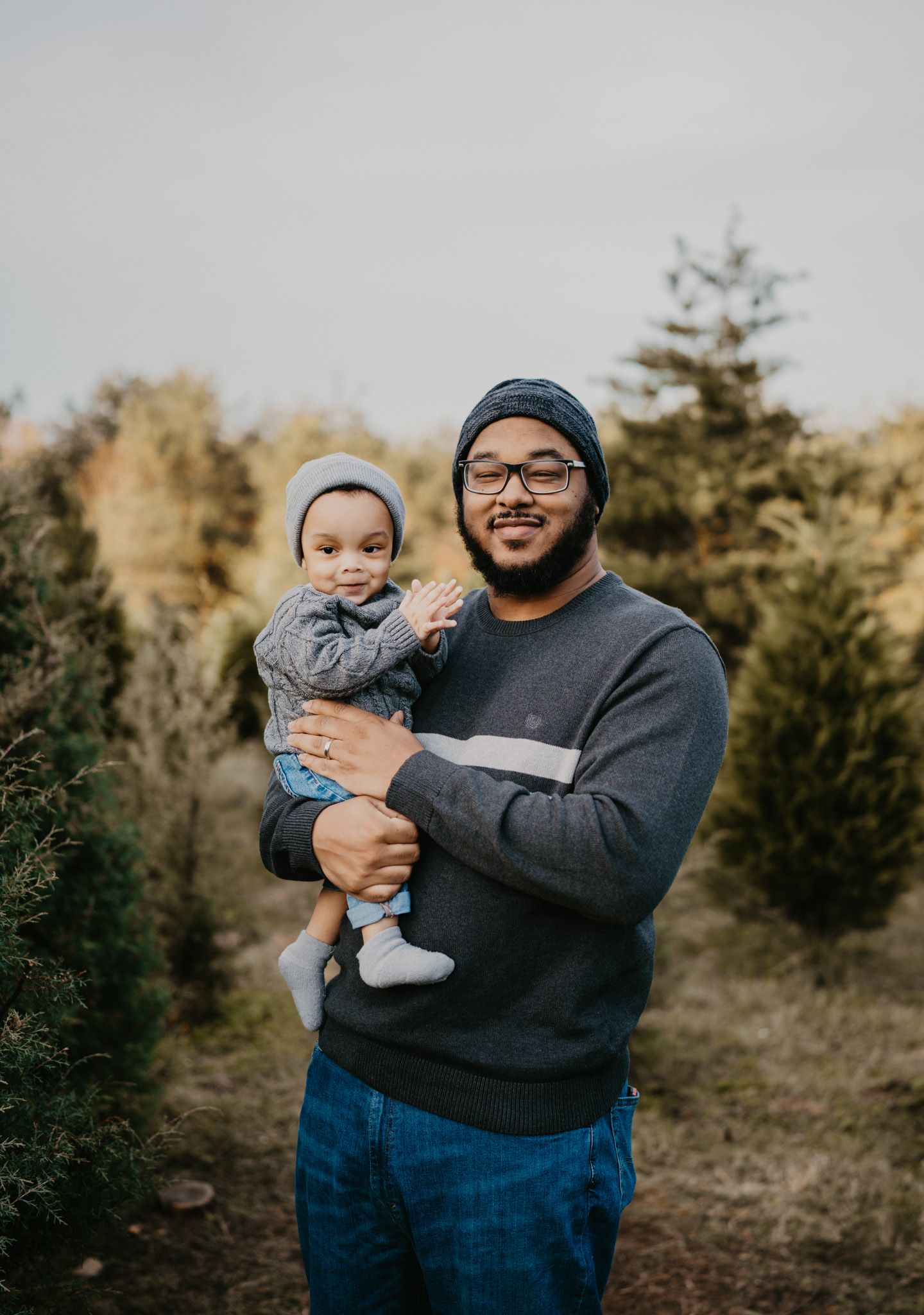 A parent and child share joyful moments together at a Christmas tree farm on a winter afternoon.