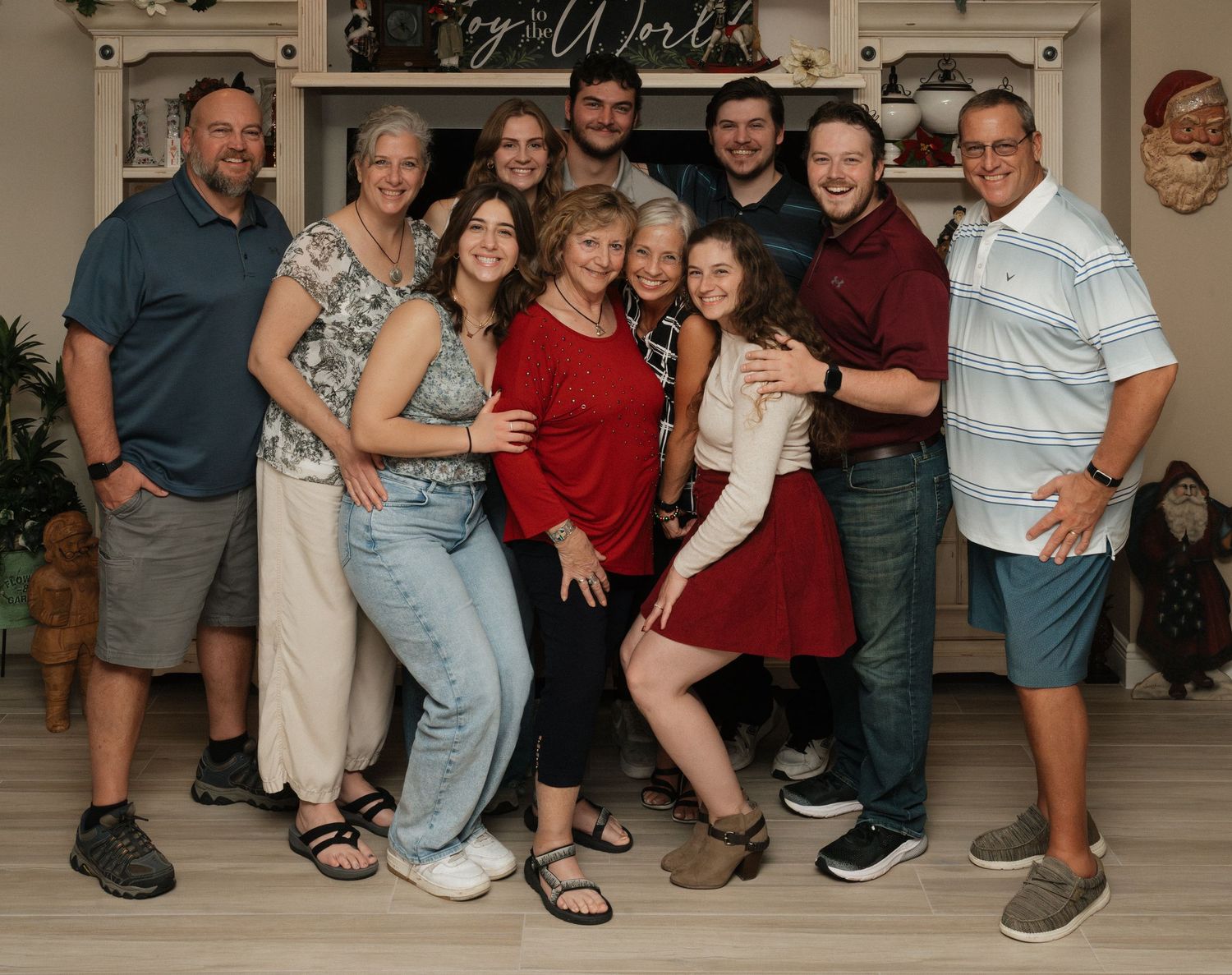A large family group poses together for a portrait in front of a decorated wall during a gathering.