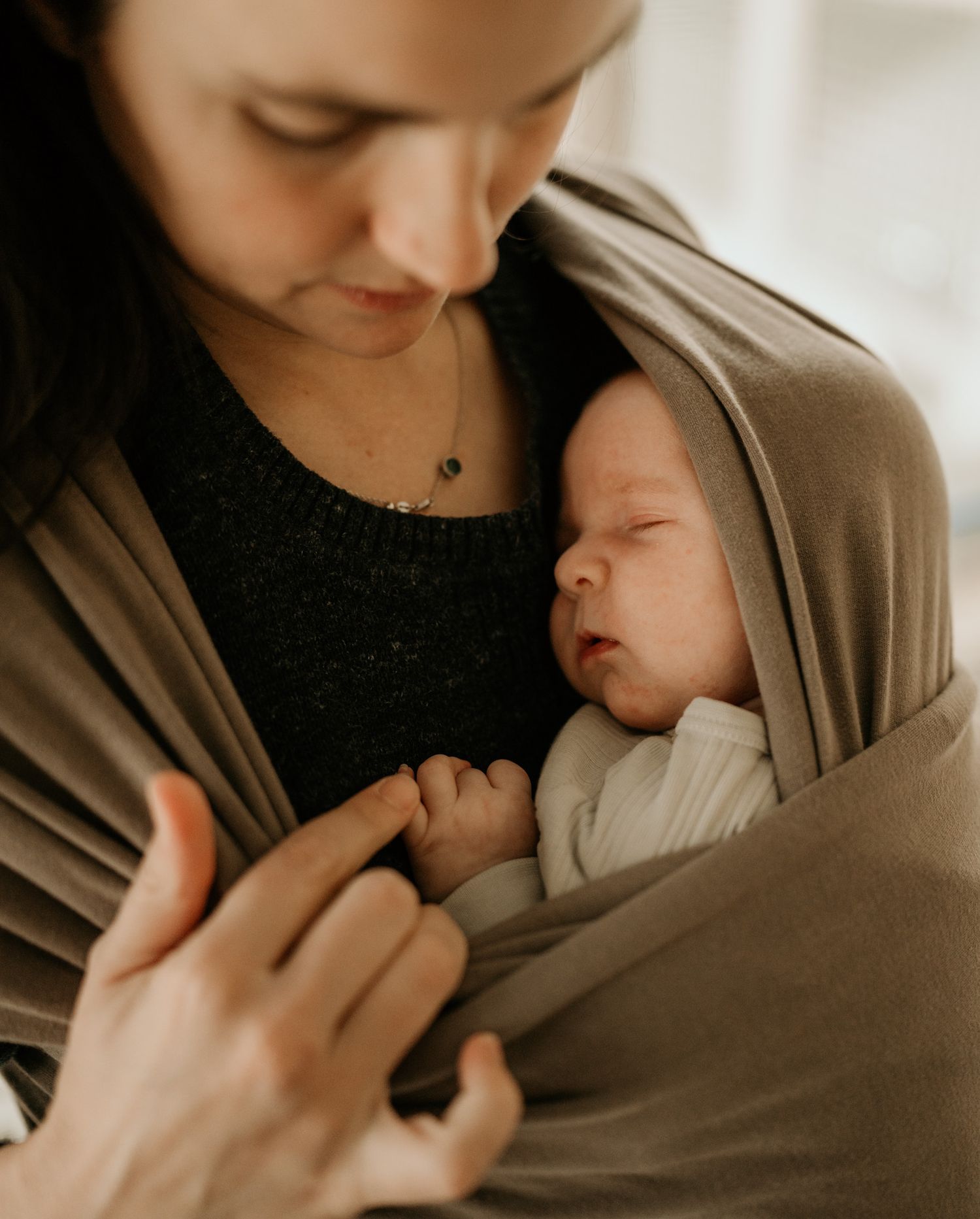 A tender moment captured in warm tones as a parent cradles and nurtures their sleeping newborn baby in a soft brown wrap.