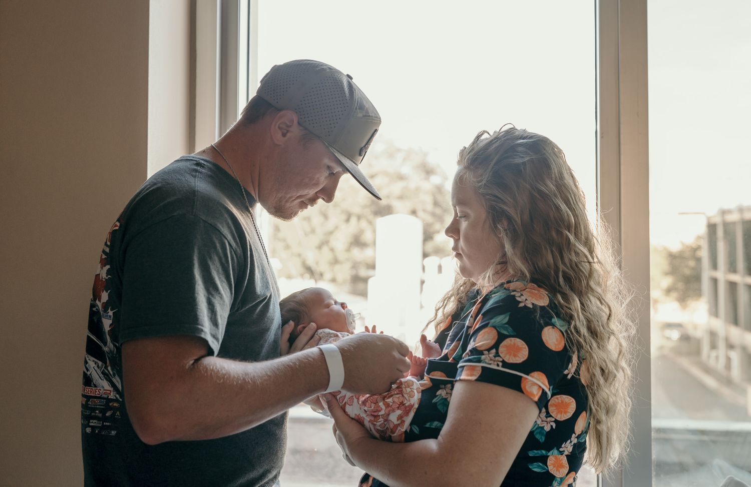 A series of candid moments showing a couple holding a baby in different poses near a window.