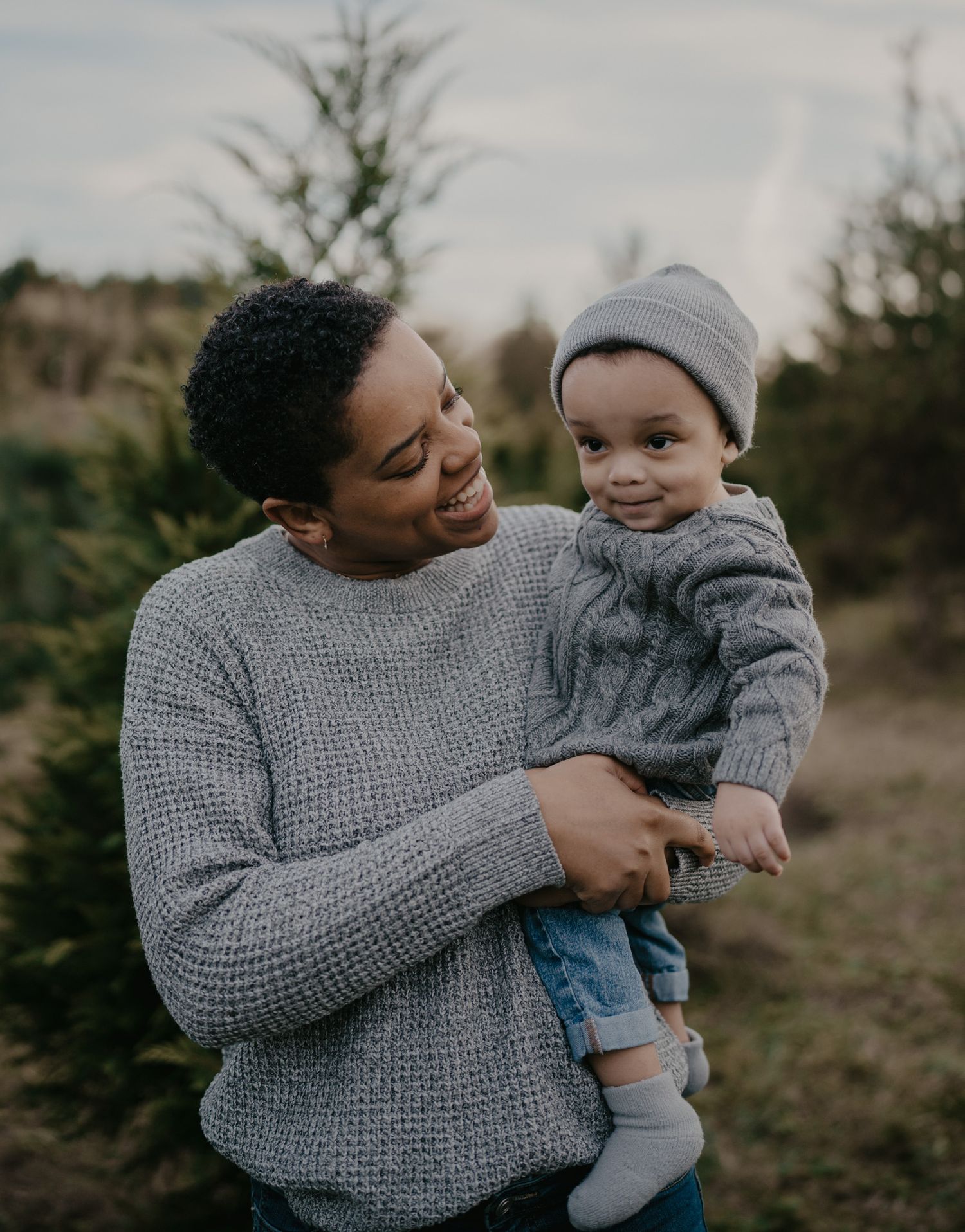 A tender moment shared between parent and baby wearing matching gray sweaters in an outdoor natural setting.