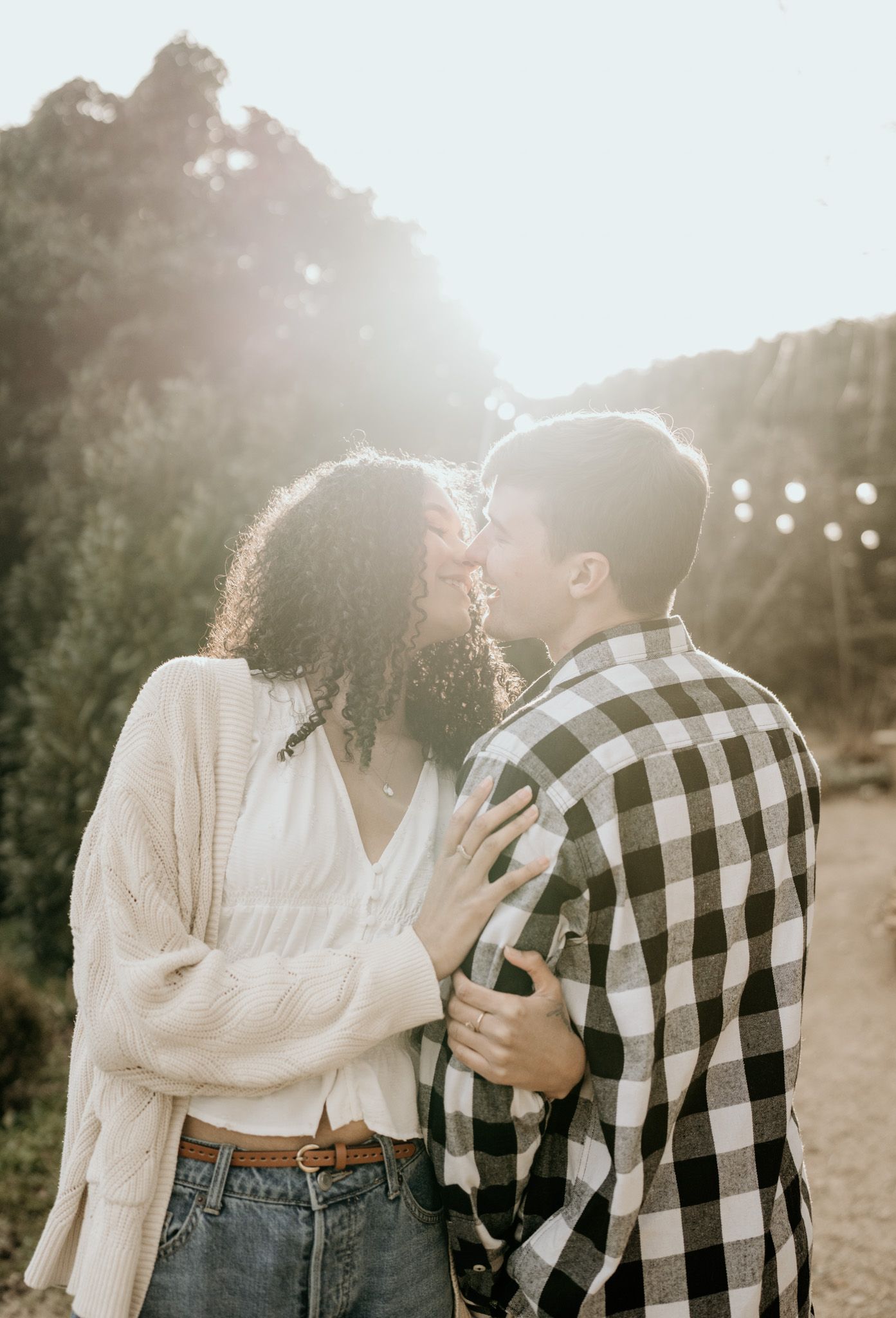 A romantic couple in casual attire shares tender moments together against a sunlit outdoor backdrop.
