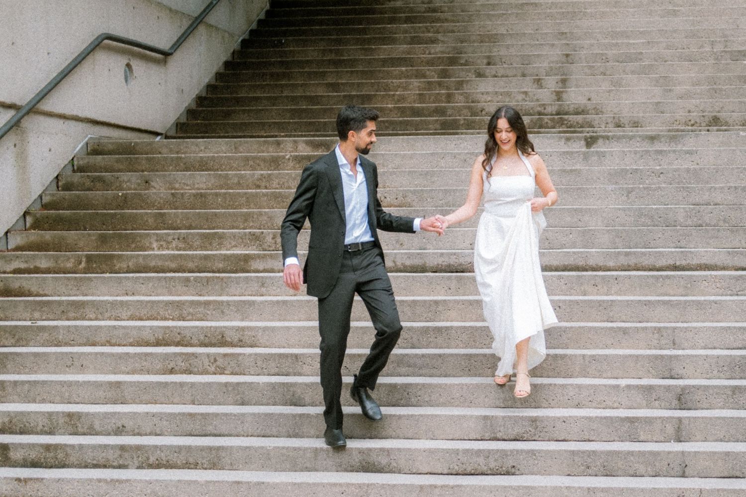 Couple in wedding attire holding hands while walking down outdoor stone steps.