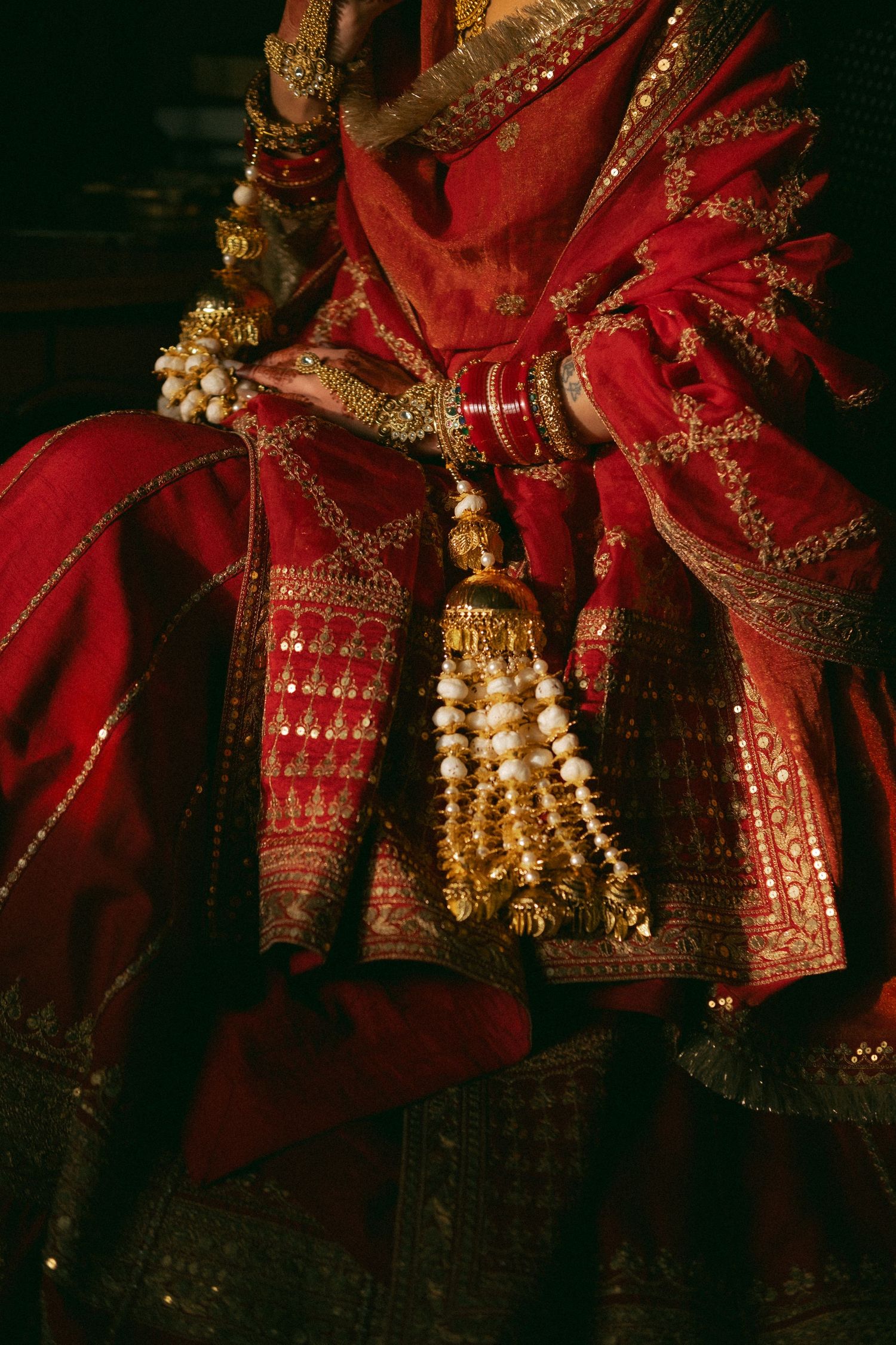 Close-up of Indian bride's hands adorned with gold bangles, kaleere, and red bridal lehenga with gold embroidery.