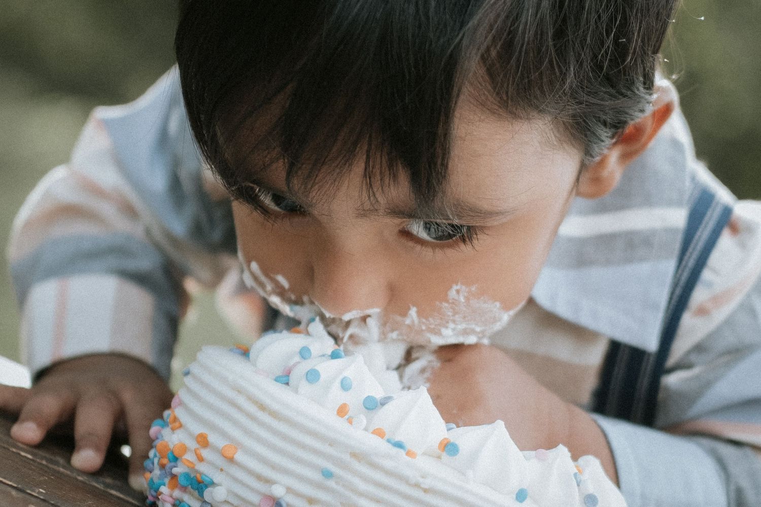 Baby boy's first birthday cake smash close-up with white frosting covering his face.
