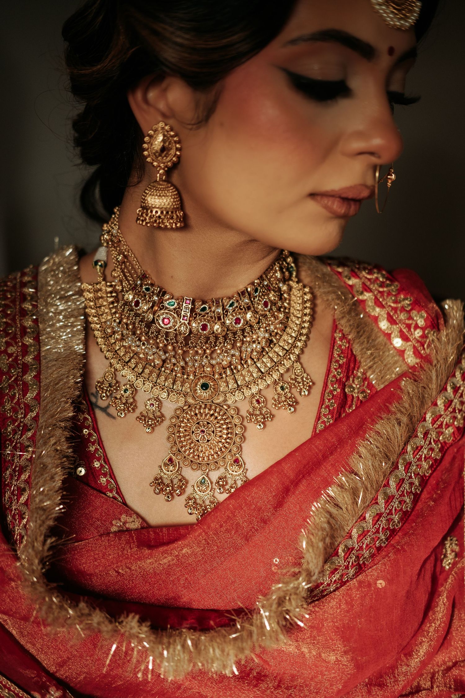 Close-up of Indian bride wearing elaborate gold kundan necklace, jhumka earrings, and red embroidered saree.
