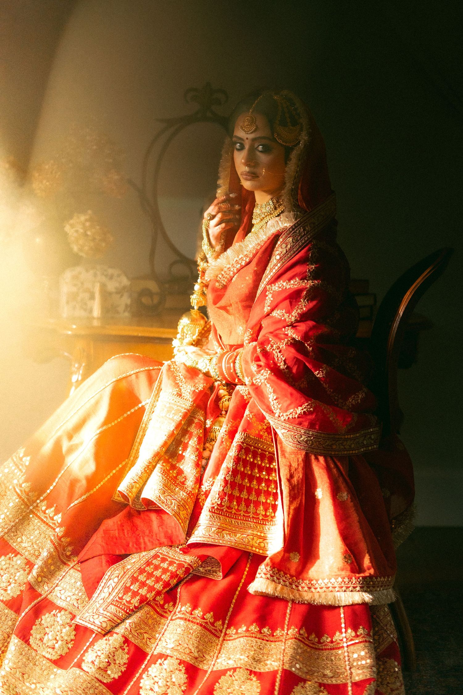 Indian bride in red and gold lehenga choli with dupatta seated in warm golden light.