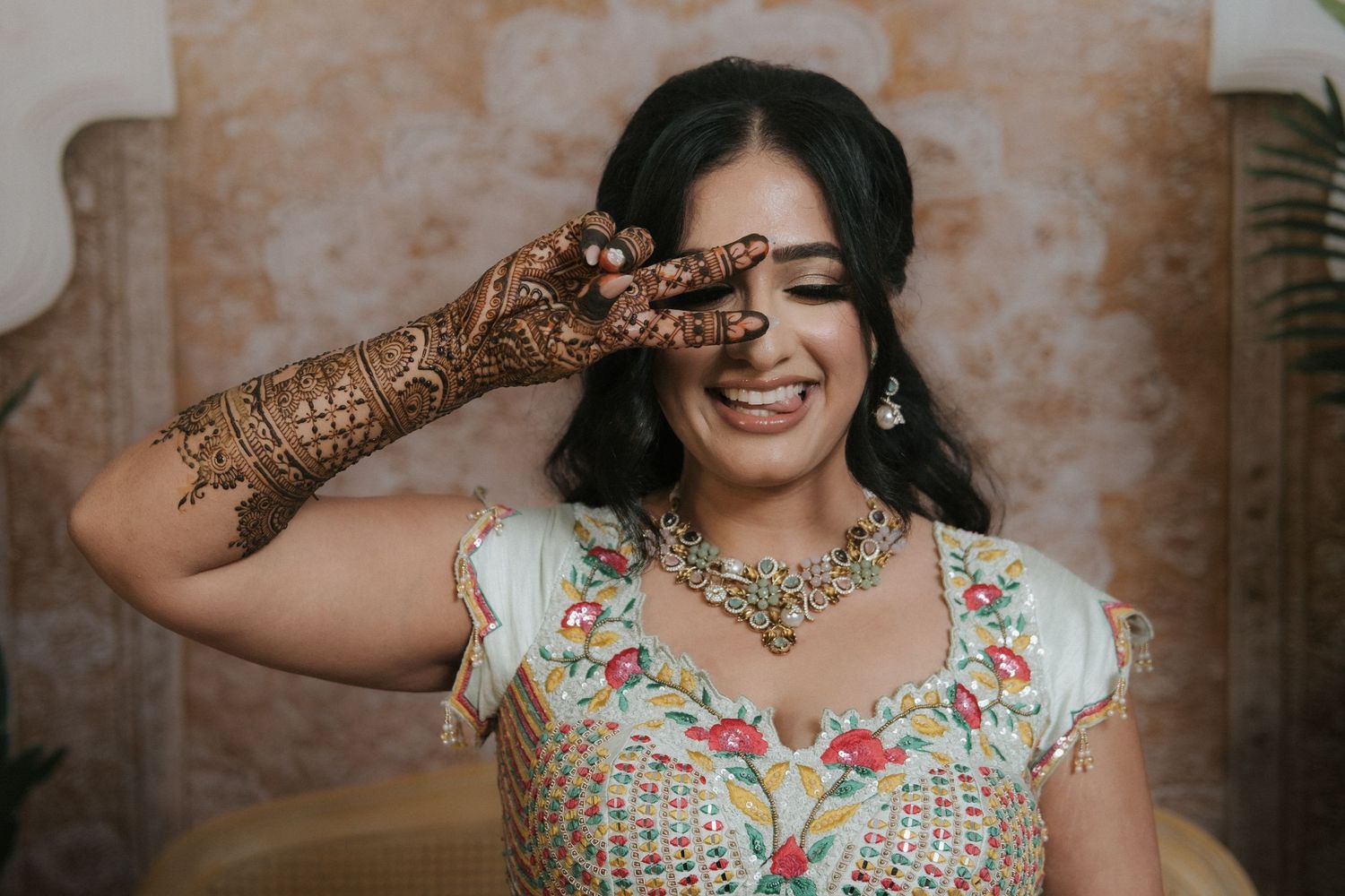 Indian bride laughing joyfully while showing intricate mehndi henna hand design, wearing colorful bridal jewelry.