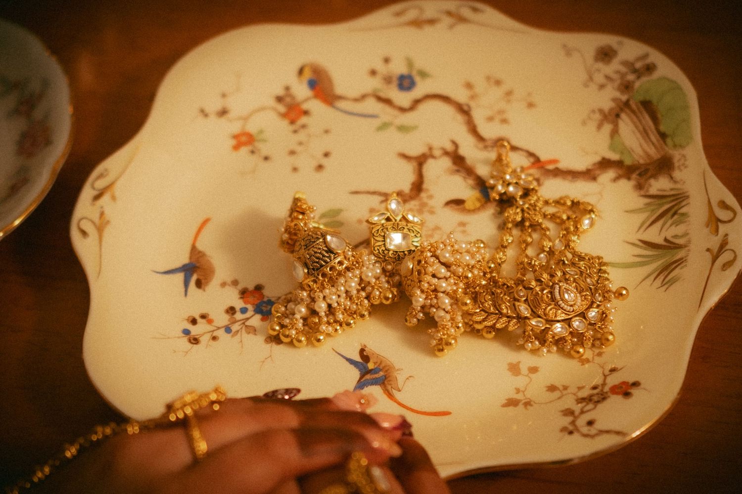 Ornate gold Indian bridal earrings displayed on a decorative white plate with floral motifs.