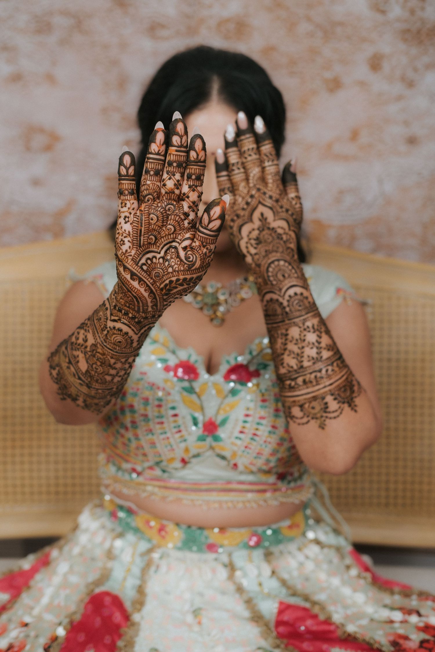 Indian bride displaying intricate bridal mehndi henna designs covering both hands and arms at wedding.