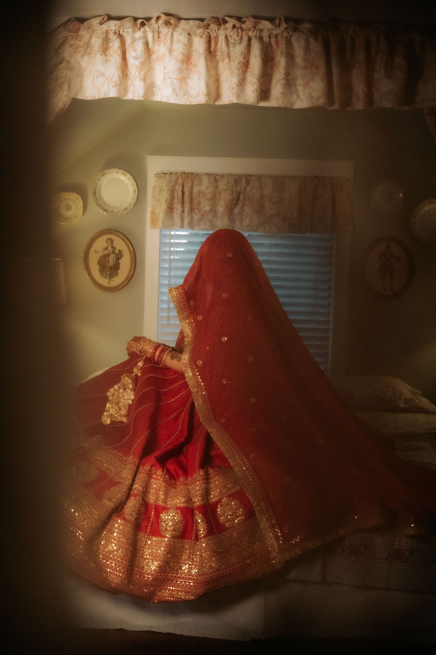 Indian bride in red gold lehenga twirling in a warmly lit vintage room with decorative plates.