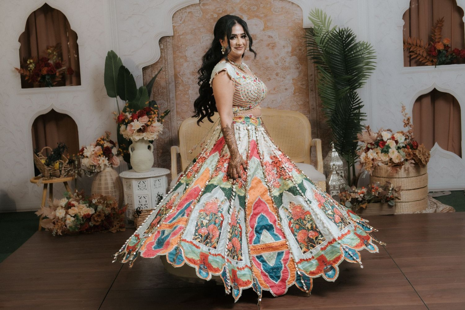 Bride twirling colorful floral lehenga in Moroccan-inspired wedding venue with tropical decor.
