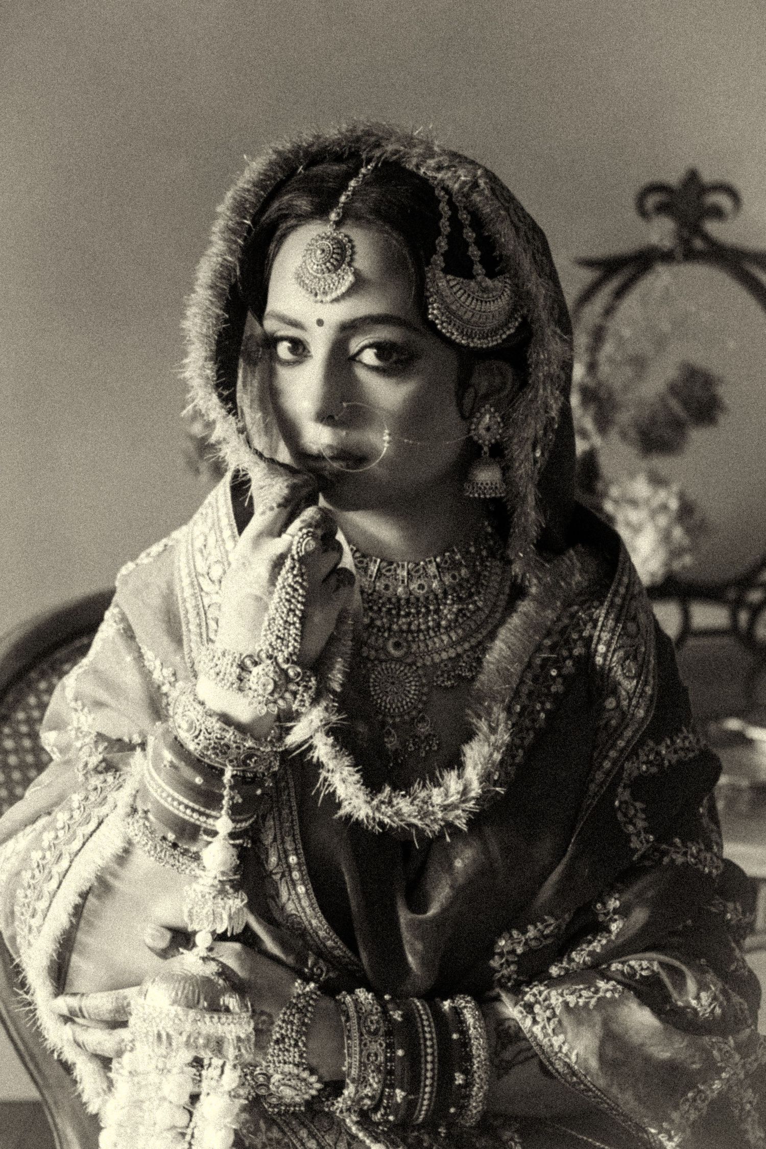 Black and white portrait of Indian bride in traditional jewelry and bridal attire looking pensive.