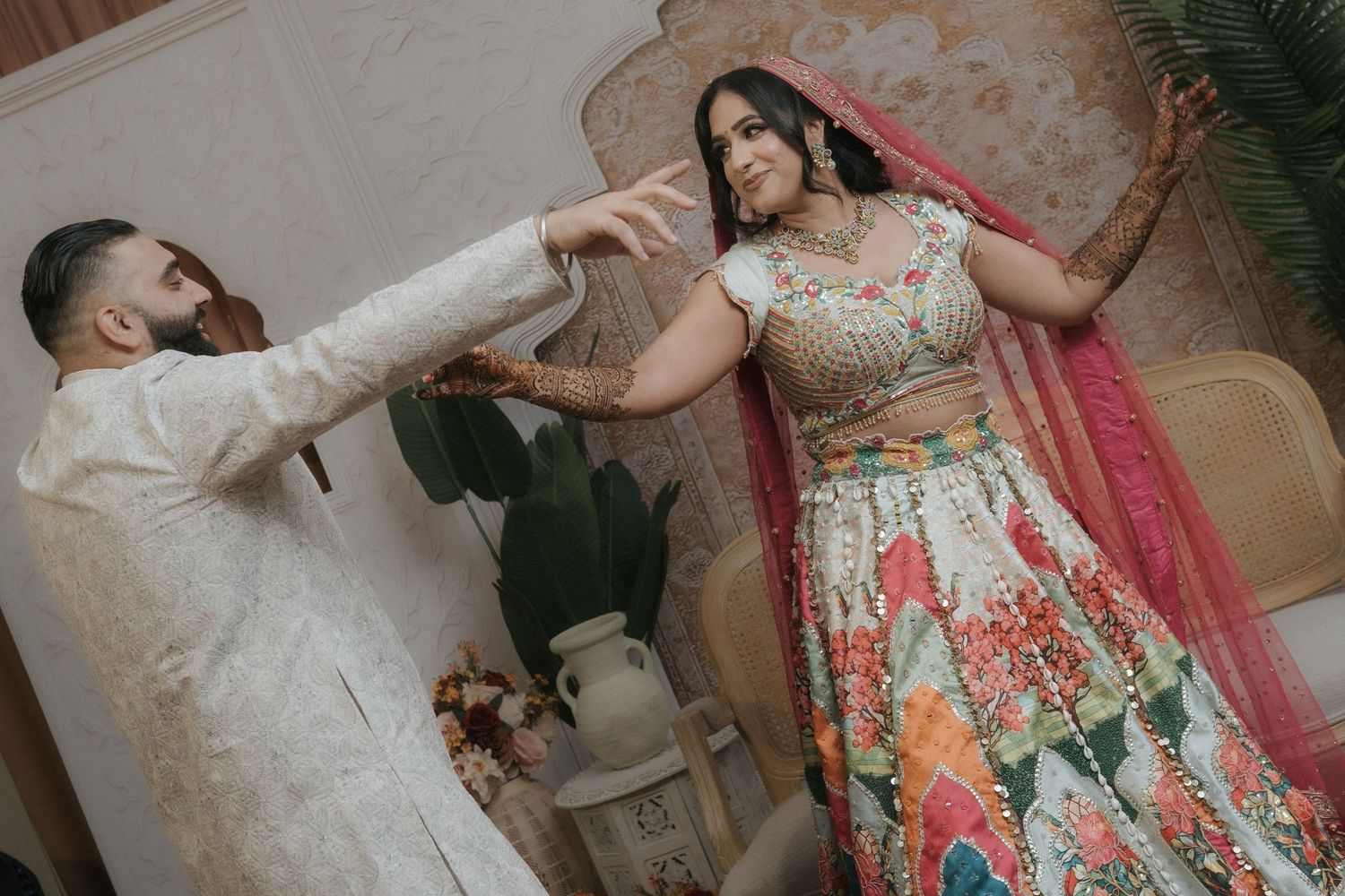 Indian groom in white sherwani playfully interacting with bride in colorful lehenga during wedding photoshoot.