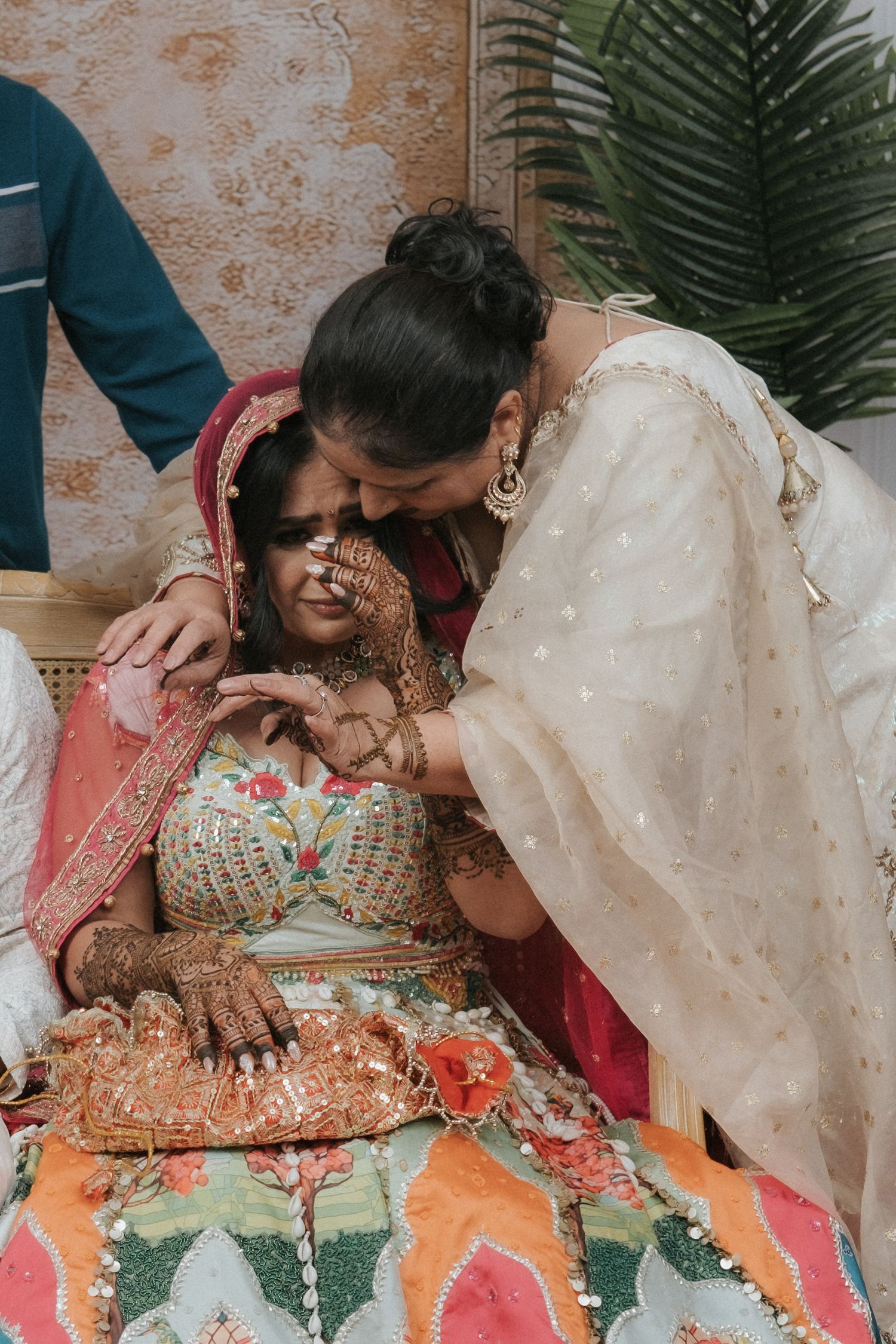 A bride in colorful lehenga with mehndi receives a tender kiss on the forehead during an Indian wedding ceremony.