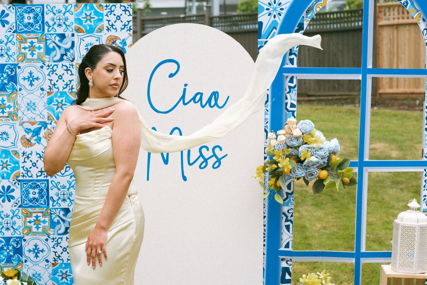 Woman in gold gown poses beside a decorative blue tile backdrop with a white arch sign reading Ciaa Miss.