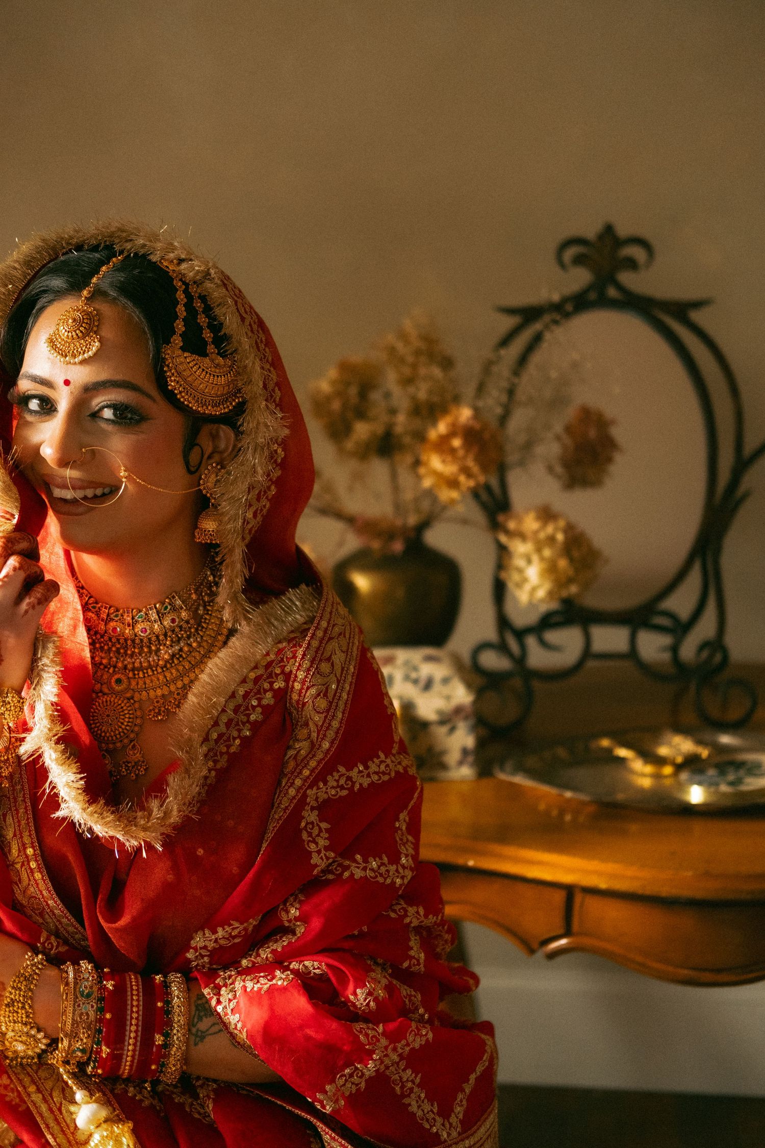 Beautiful Indian bride in red and gold lehenga sitting gracefully with ornate bridal jewelry and dupatta.