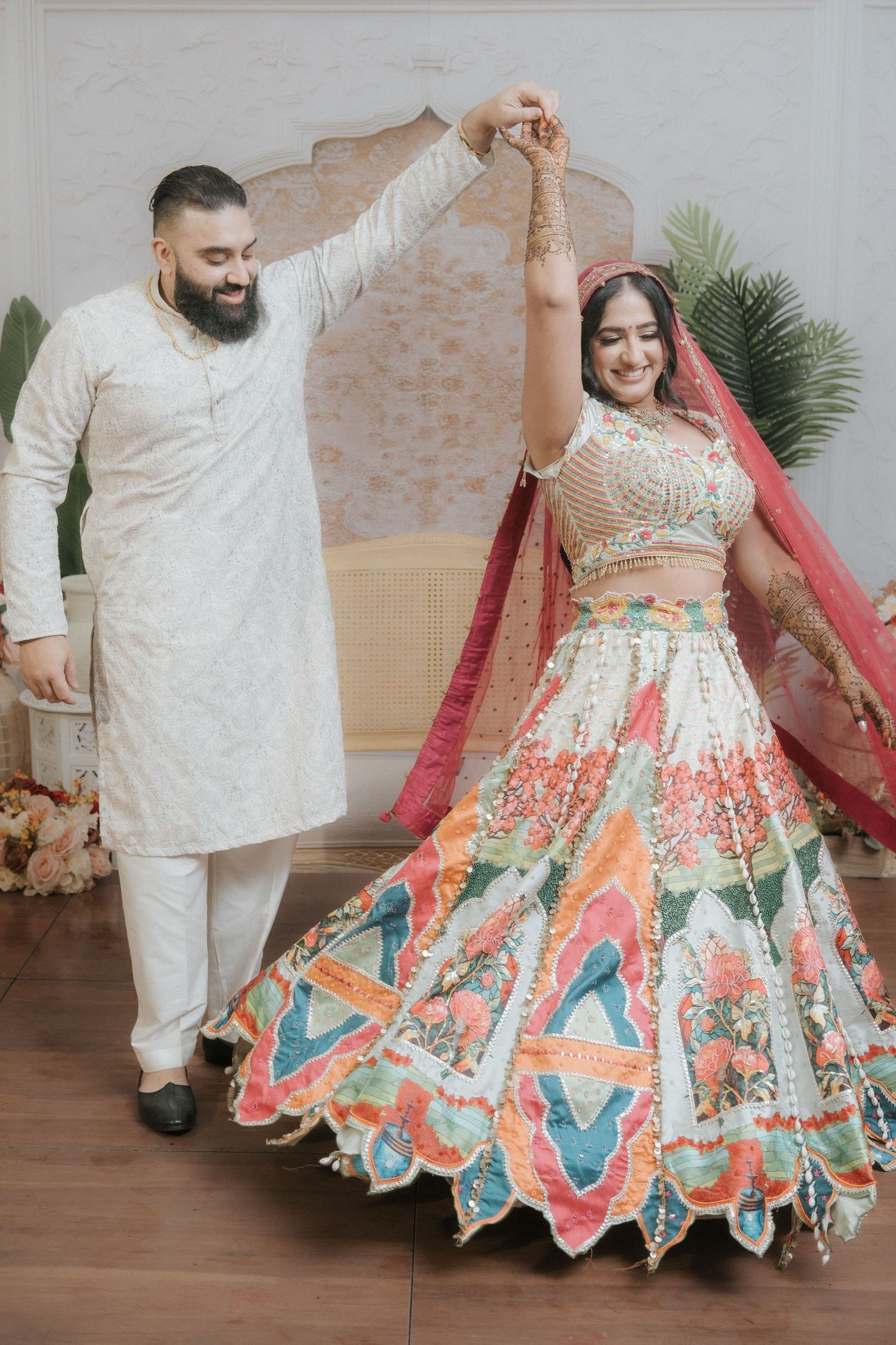 Indian groom twirling bride in vibrant multicolor floral lehenga with pink dupatta during wedding celebration.