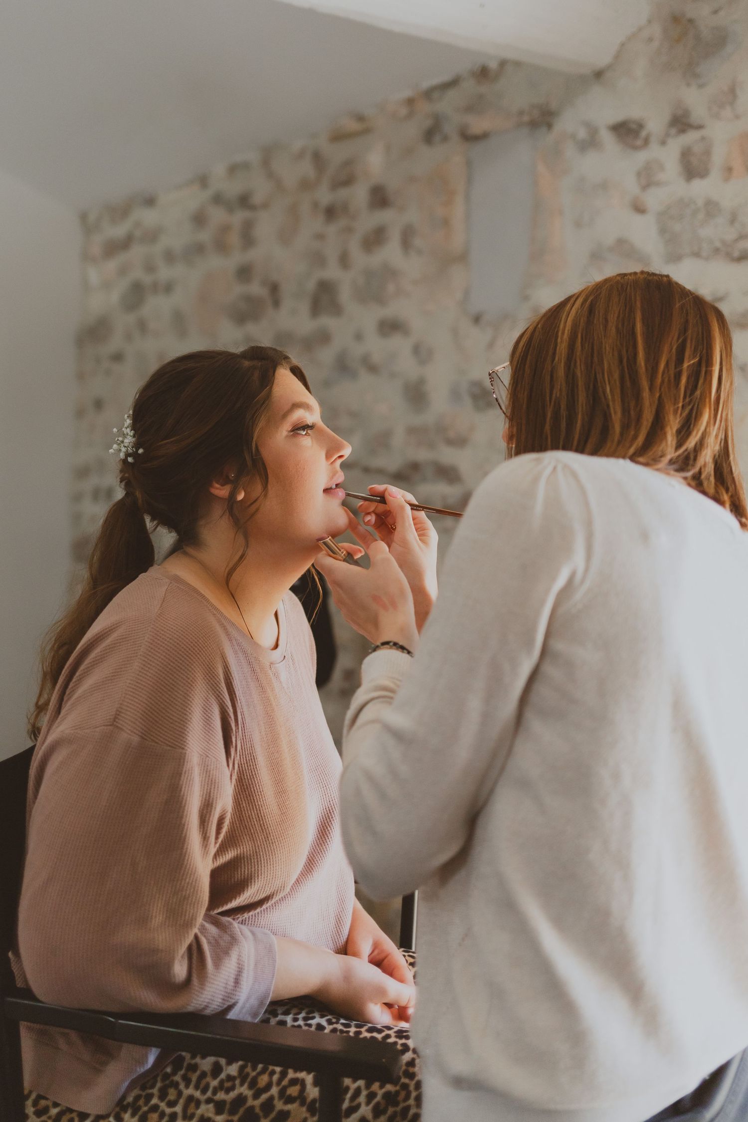Une maquilleuse professionnelle maquille une mariée pour son mariage dans un domaine de pierre. Photo par Alice Enrico, photographe Mariage