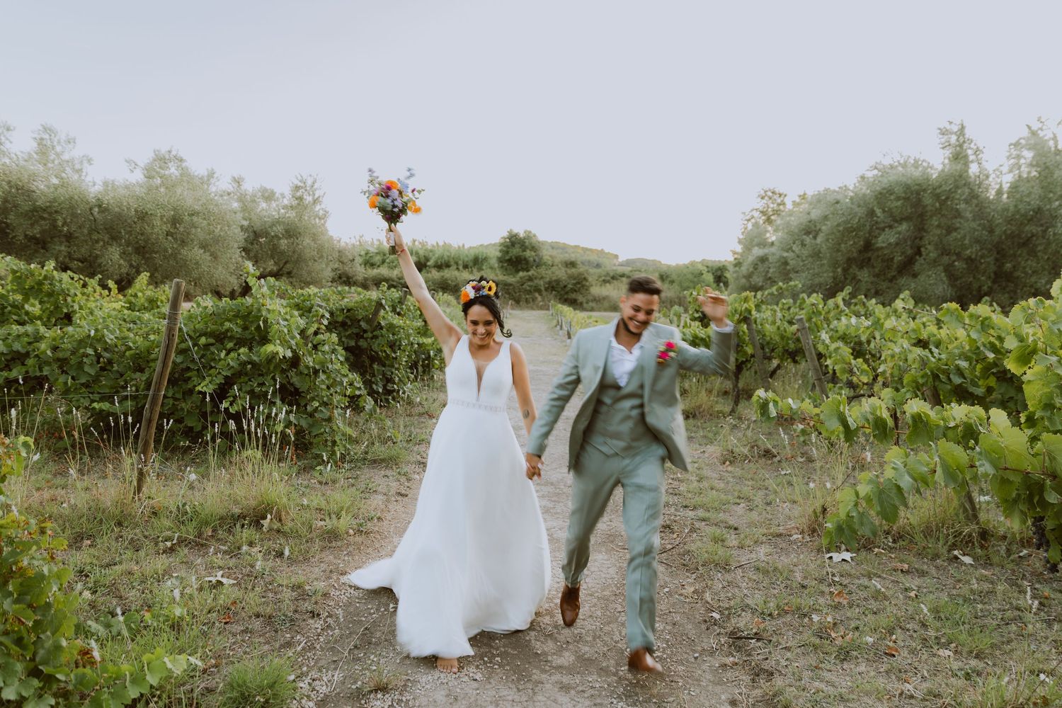 Un couple de jeunes mariés courent ensemble dans des vignes pendant leur mariage. Photo par Alice Enrico, photographe mariage à Montpellier.