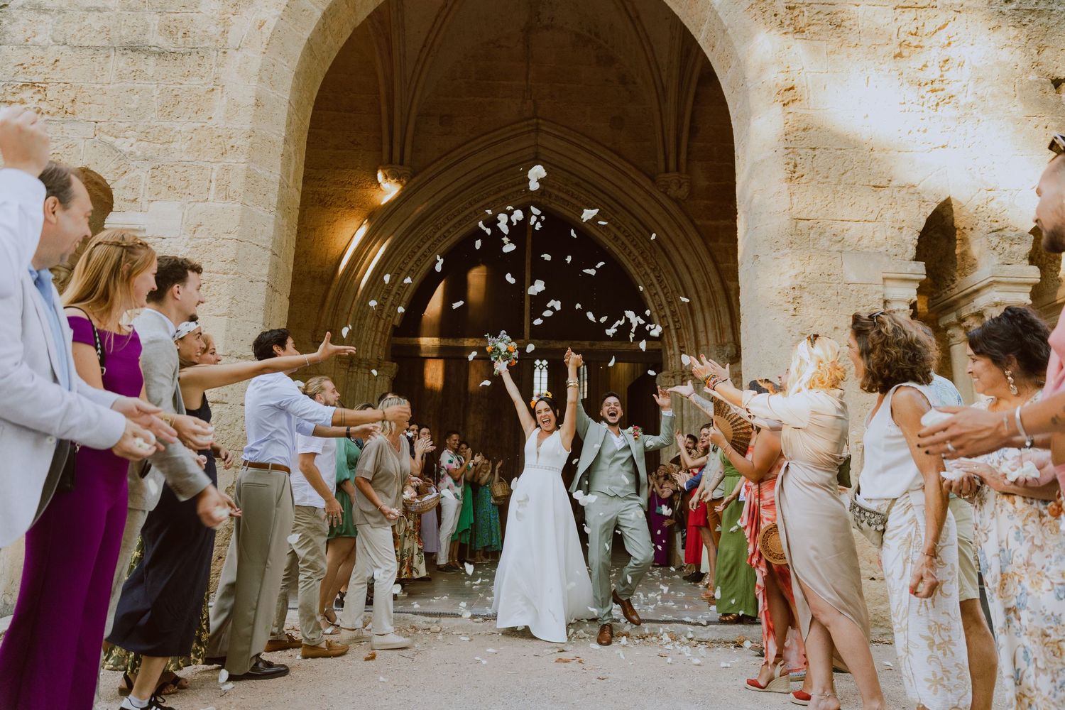 Les mariés sortent de l'église entourés de leurs proches qui jettent des pétales de fleurs. Photo par Alice Enrico, photographe Mariage à Mo