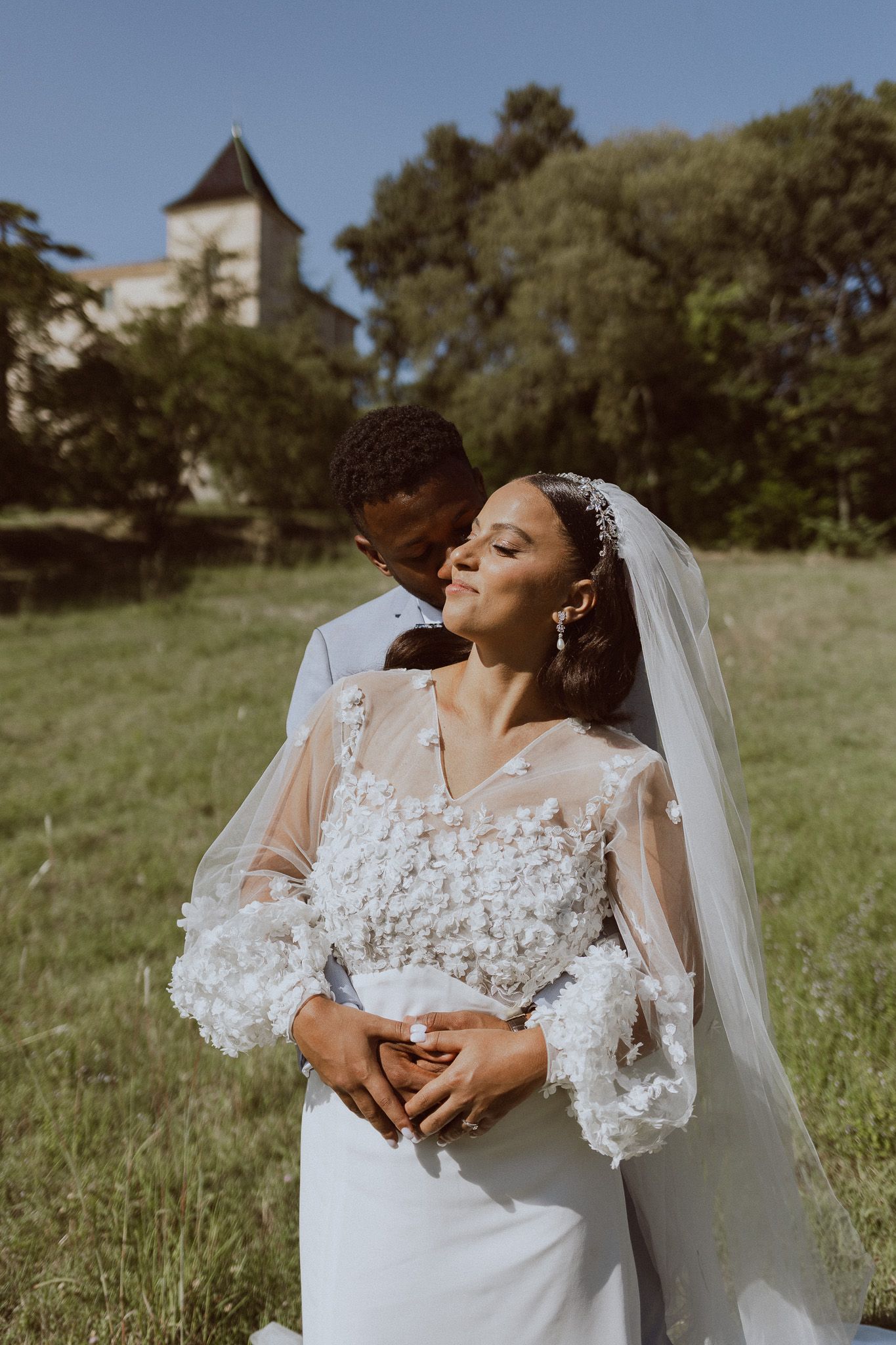 Un couple de mariés s'embrasse dans un champ devant un château. Photo par Alice Enrico, photographe mariage à Montpellier.
