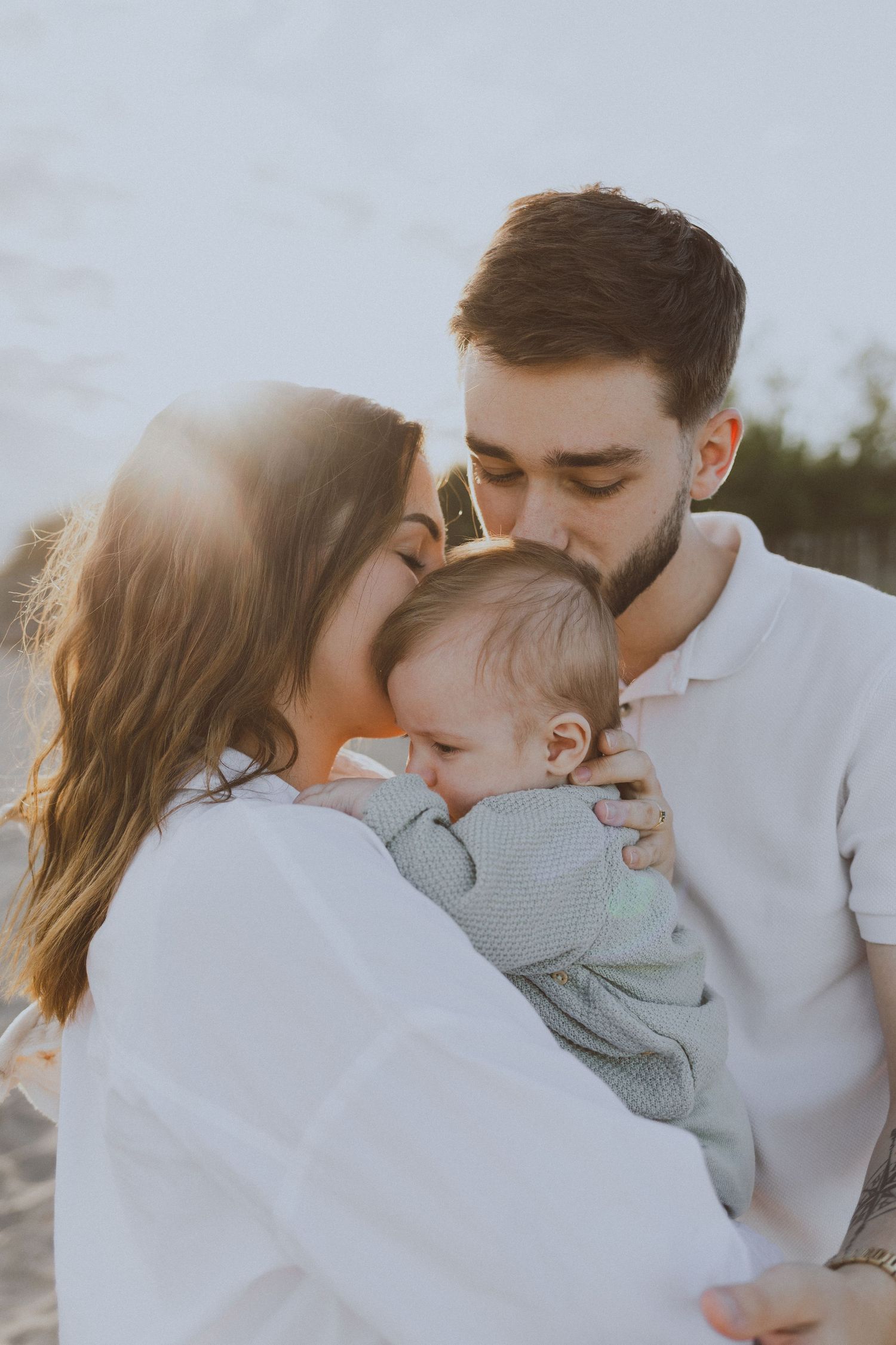 Une famille, un couple et leur bébé, se font un câlin pendant une séance photo de famille à la plage à la golden hour.