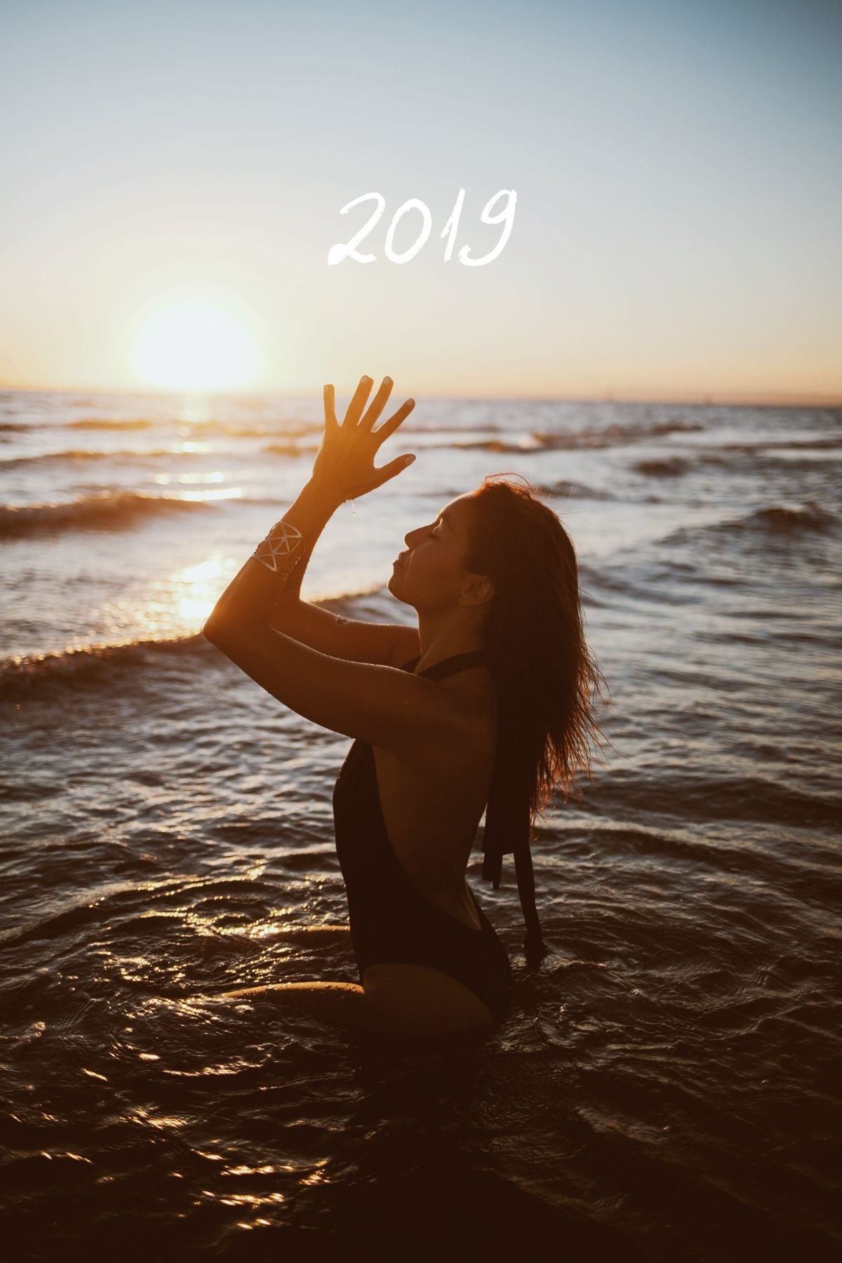 Femme lève ses mains, assise dans l'eau, au coucher de soleil, à la plage de la Grande Motte en été.