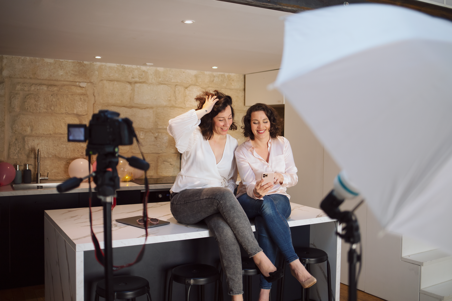 Coulisses d'un shooting photo professionnel, avec du matériel photo et vidéo, des caméras, avec deux femmes entrepreneuses souriantes.