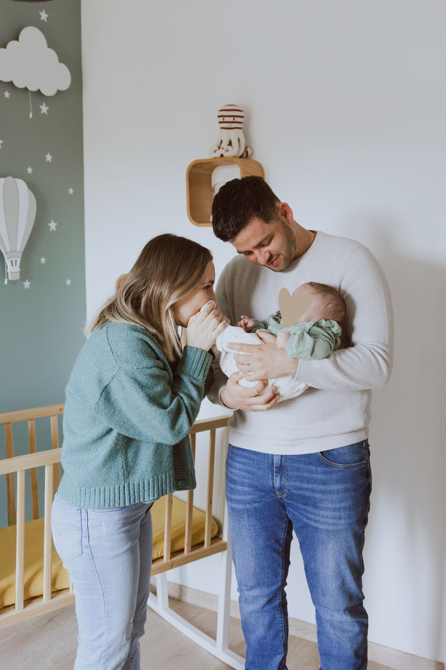 Séance photo famille à domicile, les jeunes parents jouent avec leur bébé dans sa chambre d'enfant vert sauge