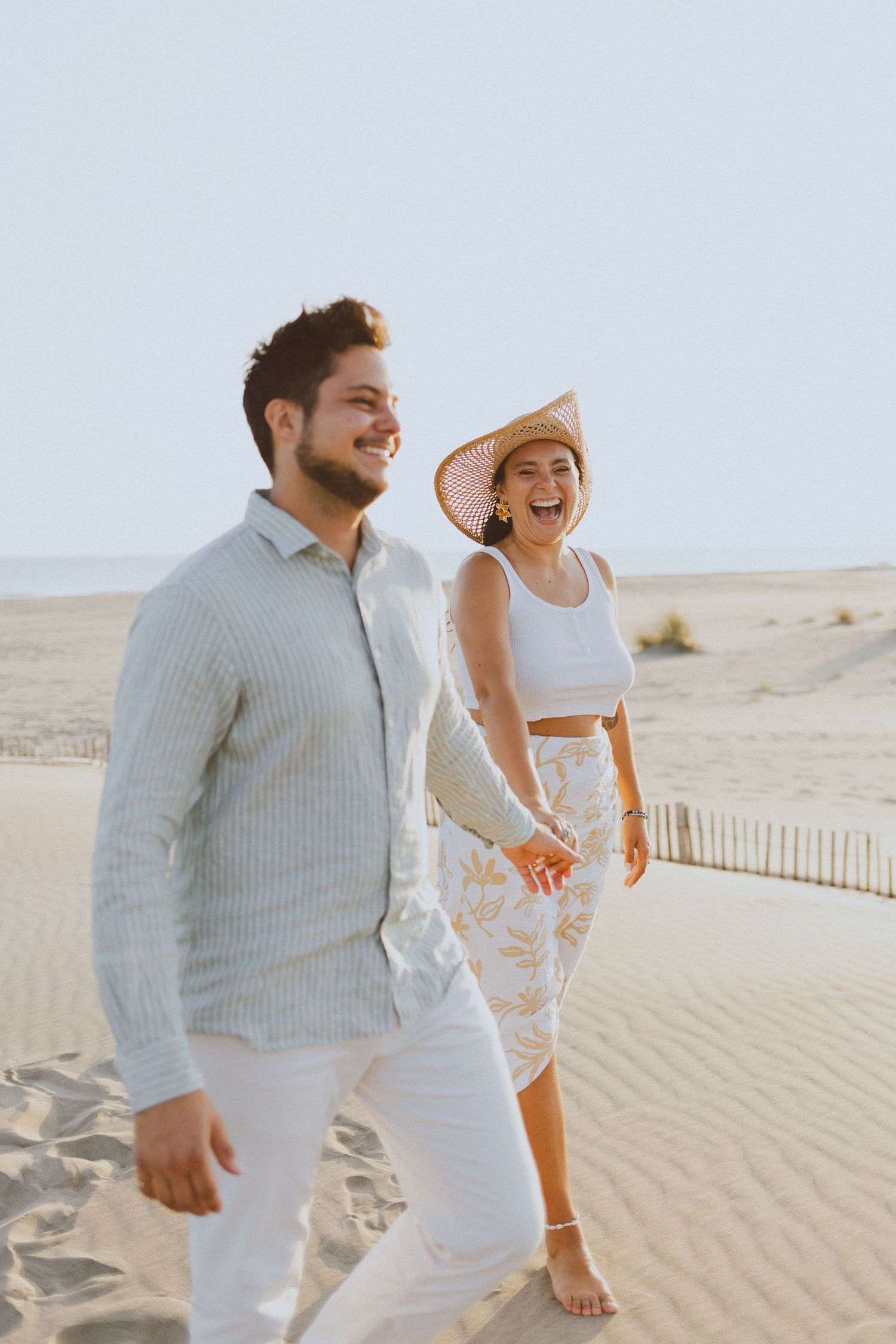 Un couple marche en ce tenant la main pendant une séance photo de couple, dans un décor de dunes de sable.