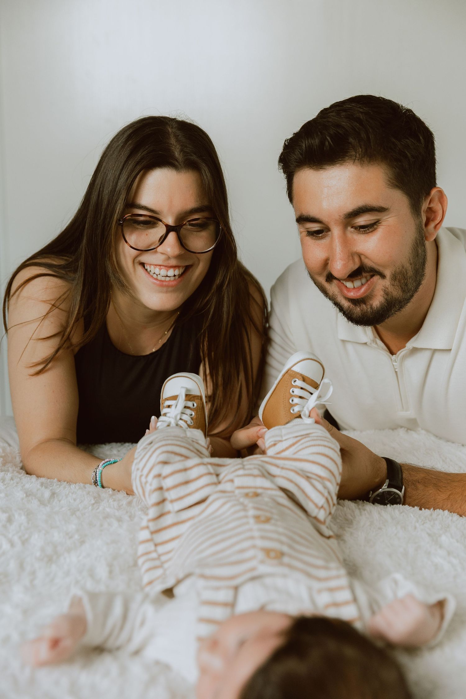 Un couple de jeunes parents regardent leur bébé avec amour lors d'une séance photo nouveau né à domicile.