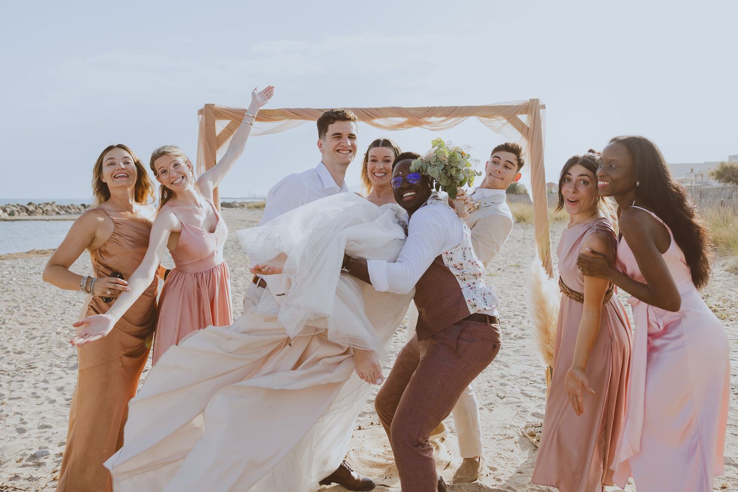 Des amies tiennent les mariés en rigolant pendant la séance photo de groupe. Photo par Alice Enrico, photographe mariage à Montpellier.