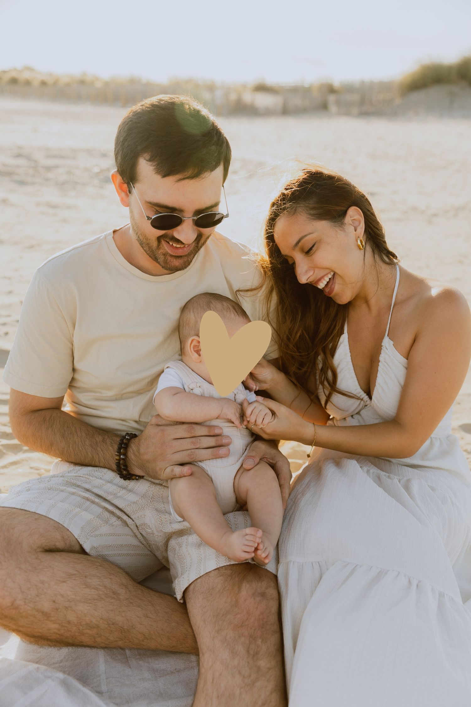 Un jeune couple joue avec son bébé à la plage à la golden hour assis sur le sable