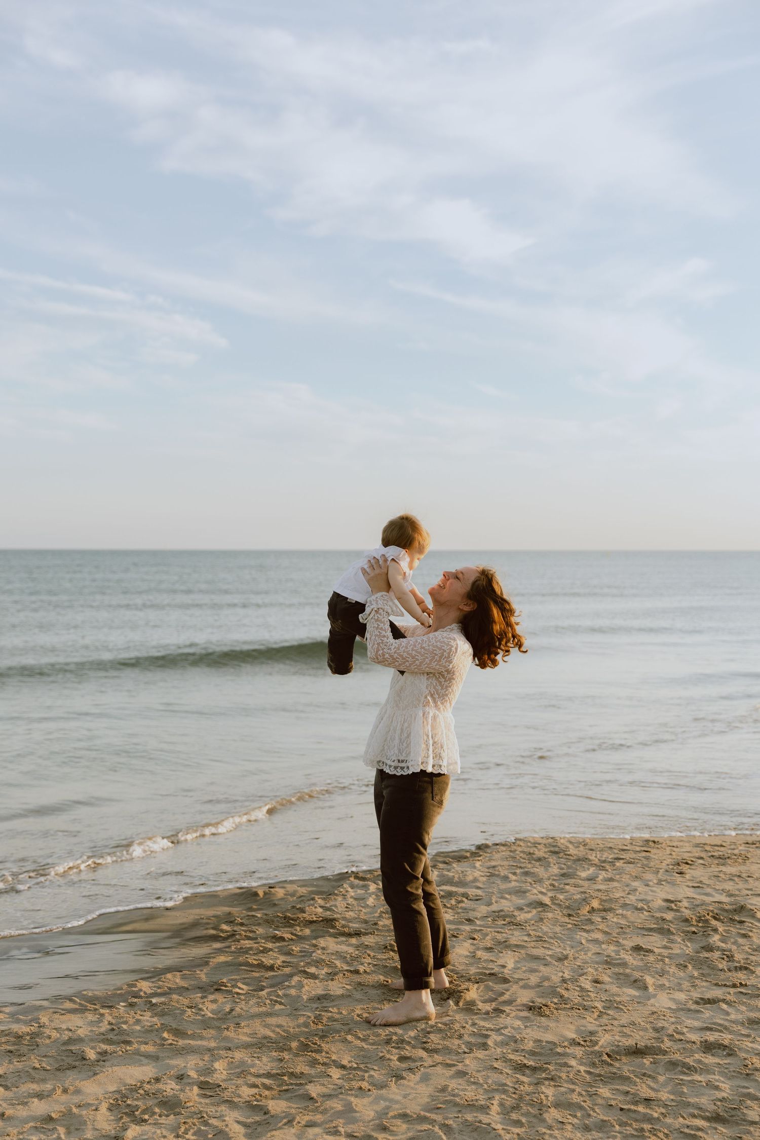 Une maman joue avec sa petite fille au bord de la mer lors d'un shooting en famille.