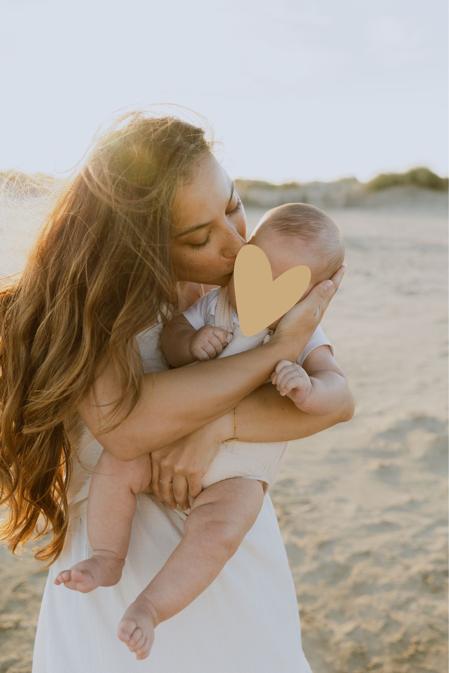 Une maman embrasse son nouveau né pendant une séance photo à la plage à la golden hour.