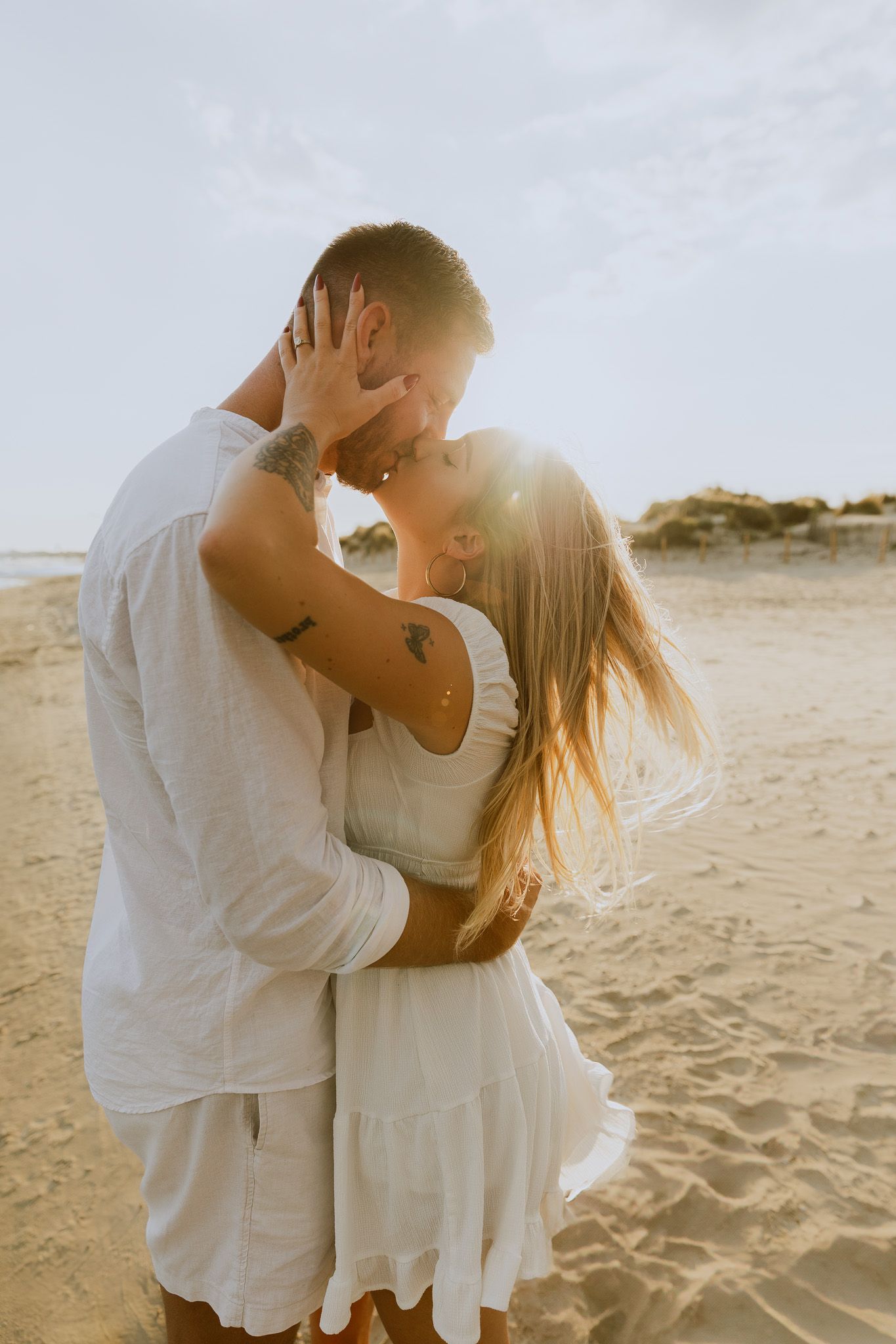 Un couple s'embrasse au bord de l'eau à la plage de Frontignan pendant leur séance photo d'engagement au coucher de soleil.