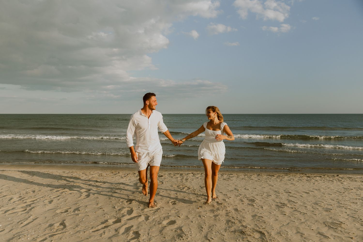 Un couple court vers l'objectif main dans la main, à la plage, lors d'une séance photo en couple