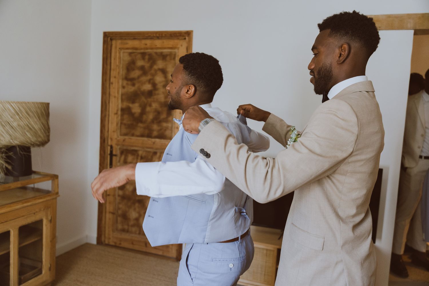 Le marié se prépare dans une chambre du domaine avec son témoin qui l'aidé à s'habiller. Photo par Alice Enrico, photographe mariage à Montp