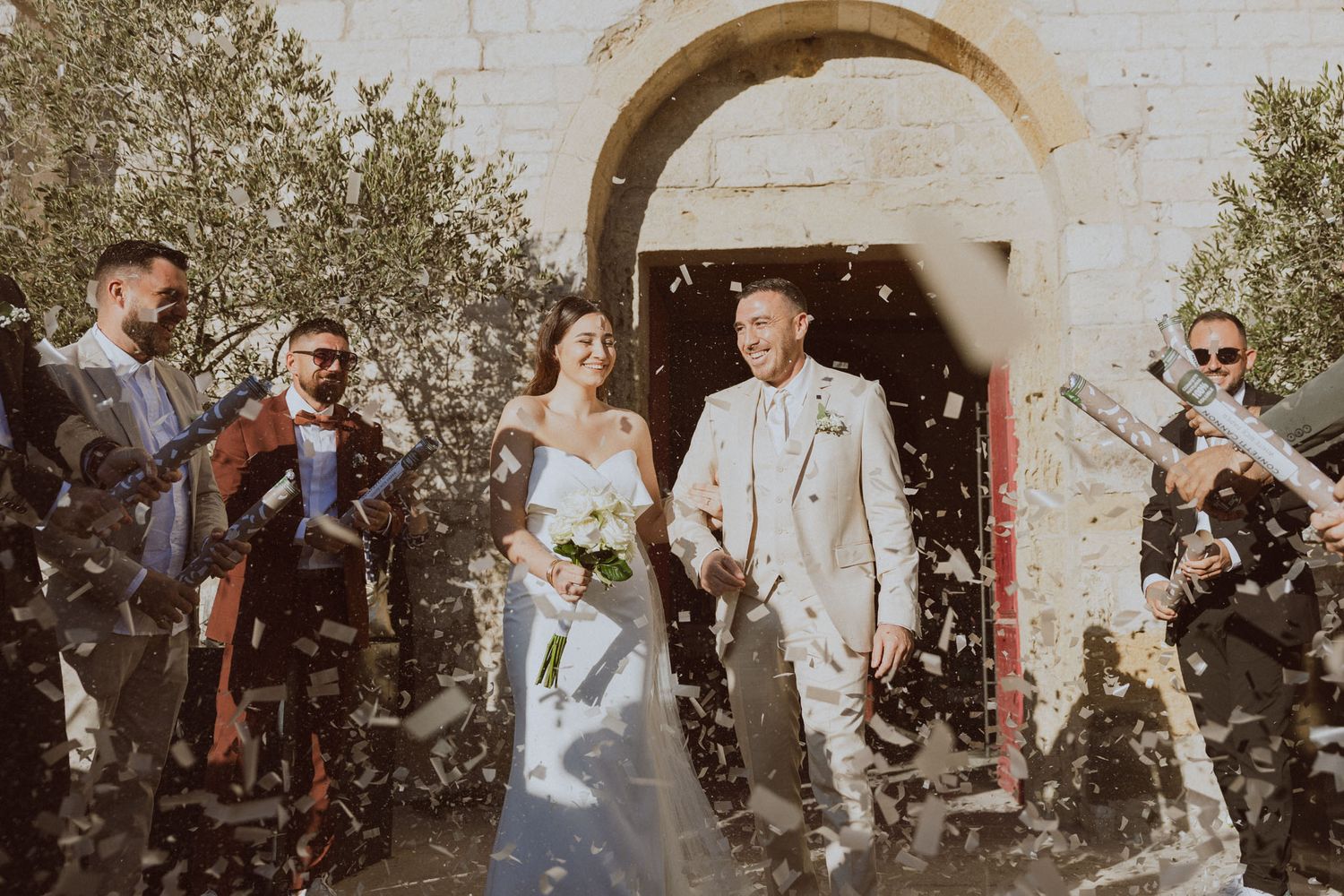 Un couple de jeunes mariés sort de l'église après la cérémonie souriants et entourés de leurs proches. Photo par Alice Enrico, photographe M