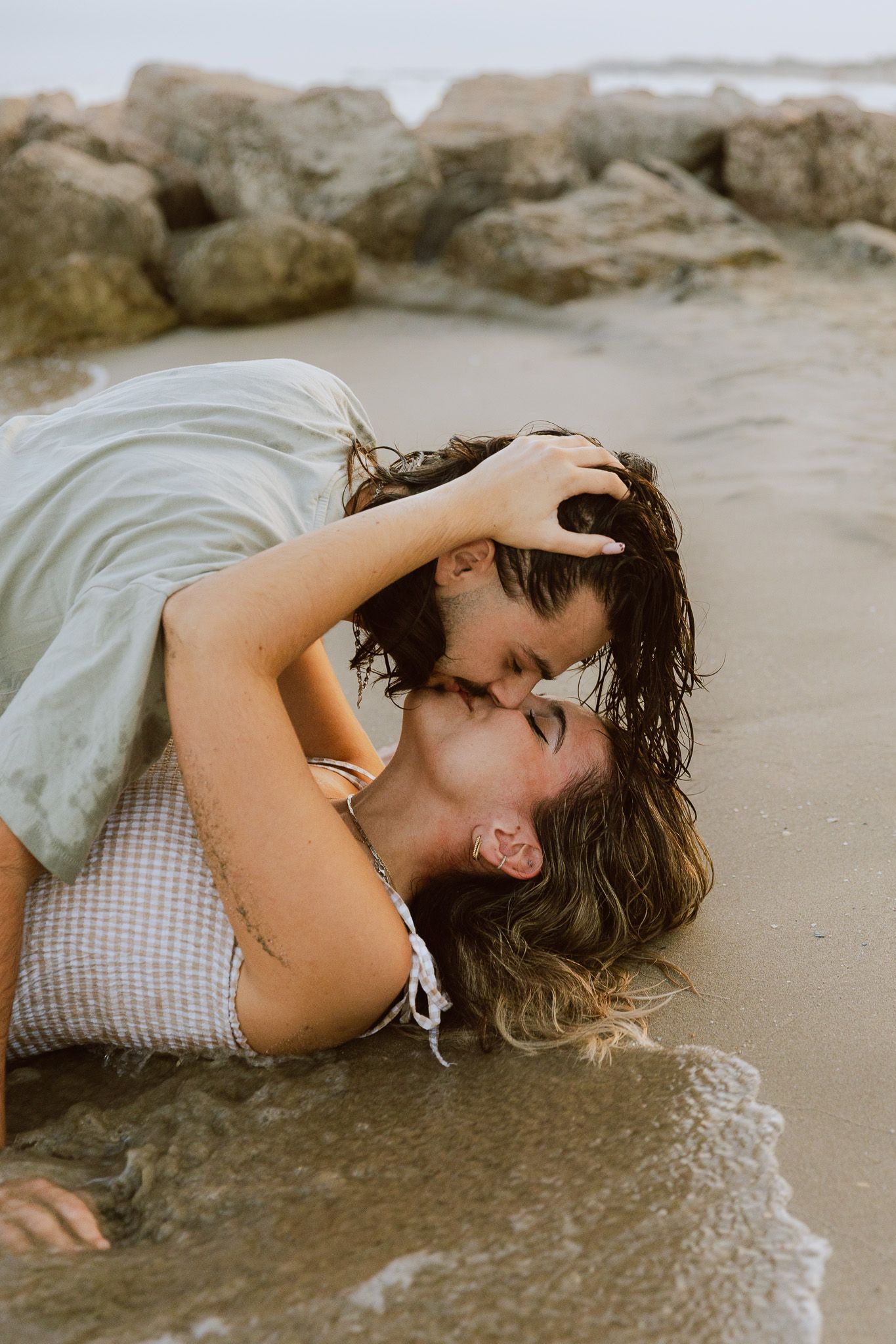 Un couple s'embrasse passionnément sur le sable pendant une séance photo de couple.
