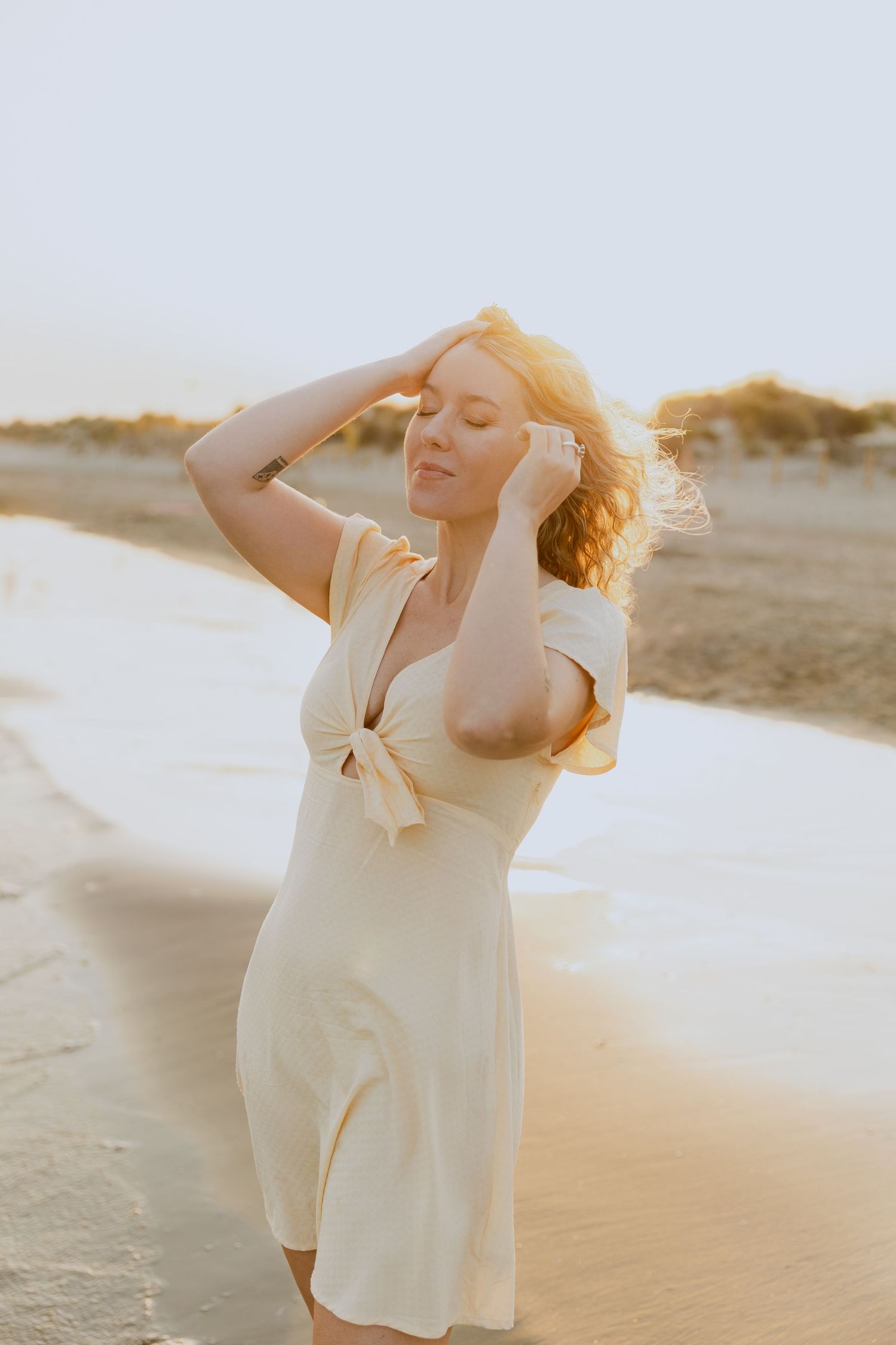 Une jeune fille en robe jaune pose au bord de la mer pendant une séance photo au coucher de soleil.