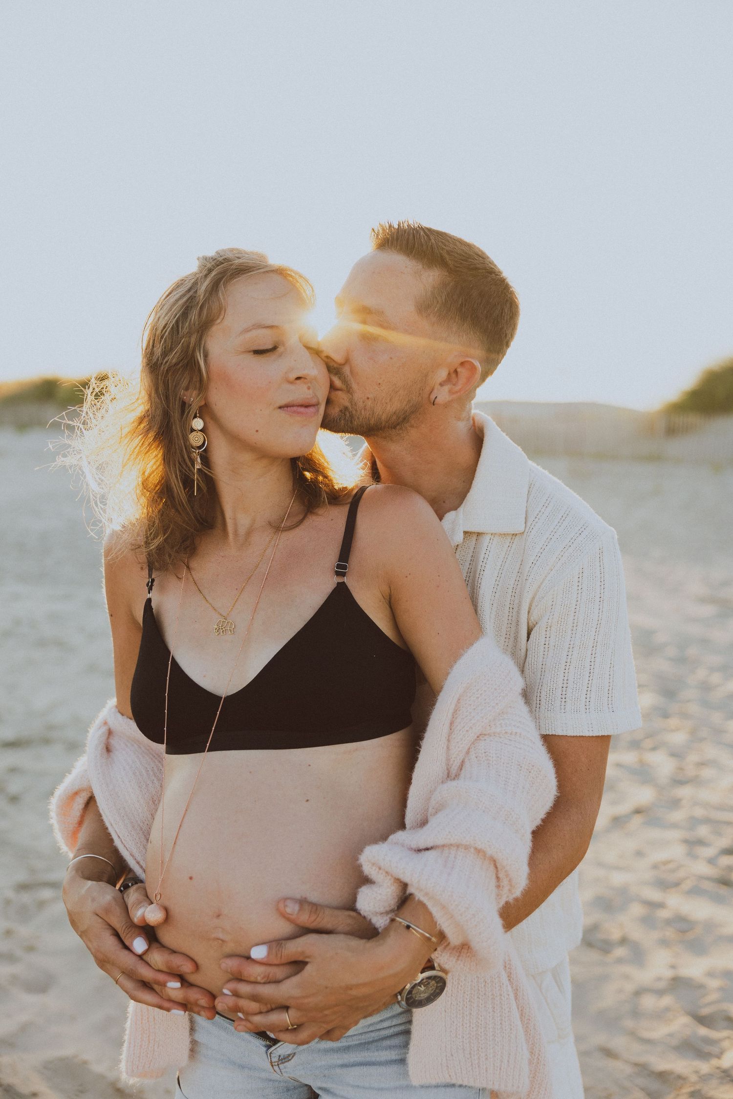 Un couple s'embrasse pendant une séance photo de grossesse à la golden hour à la plage.