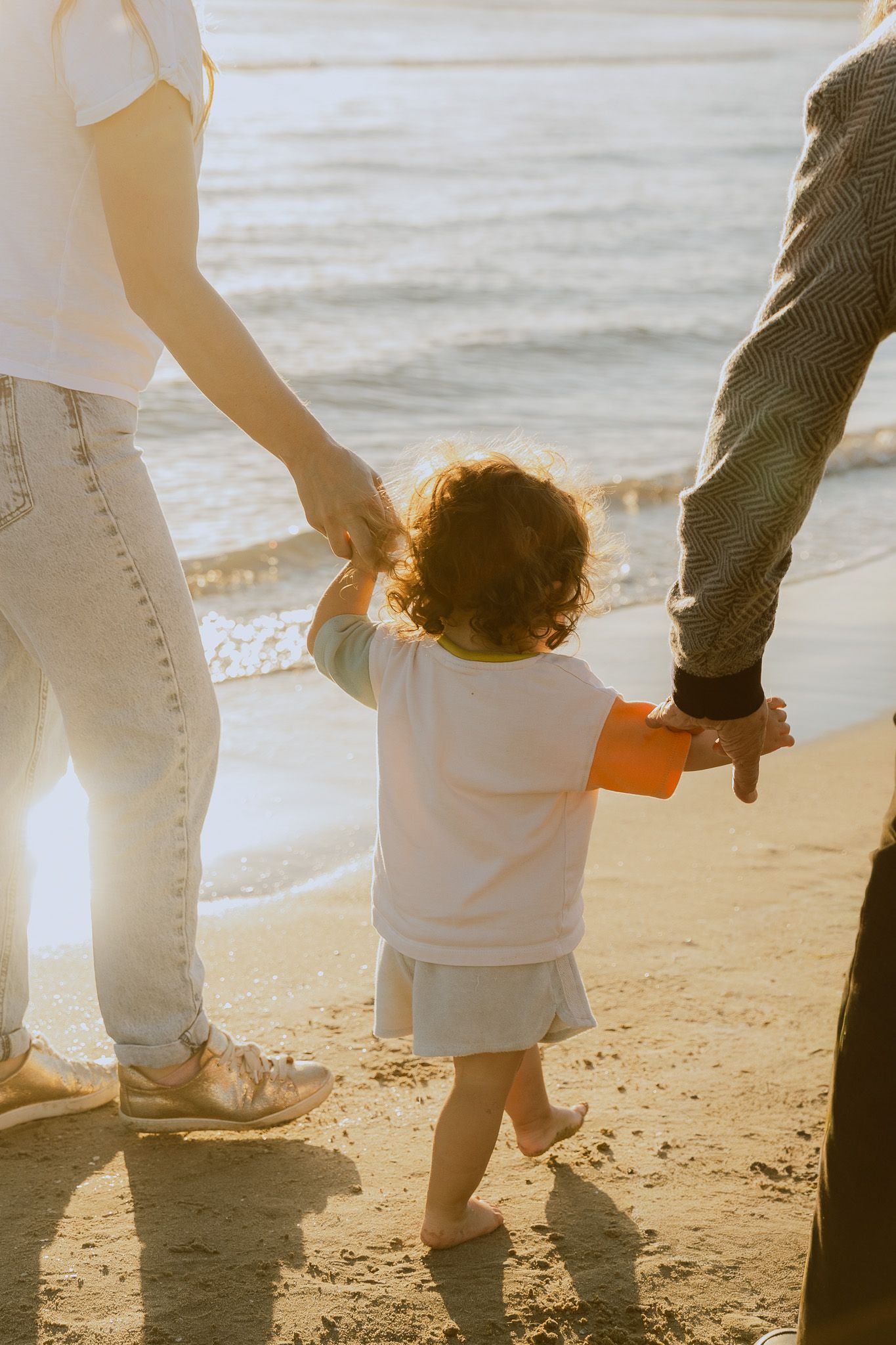 Des mains de parents qui tiennent leur bébé pendant un shooting photo en famille à la golden hour à la Grande Motte.
