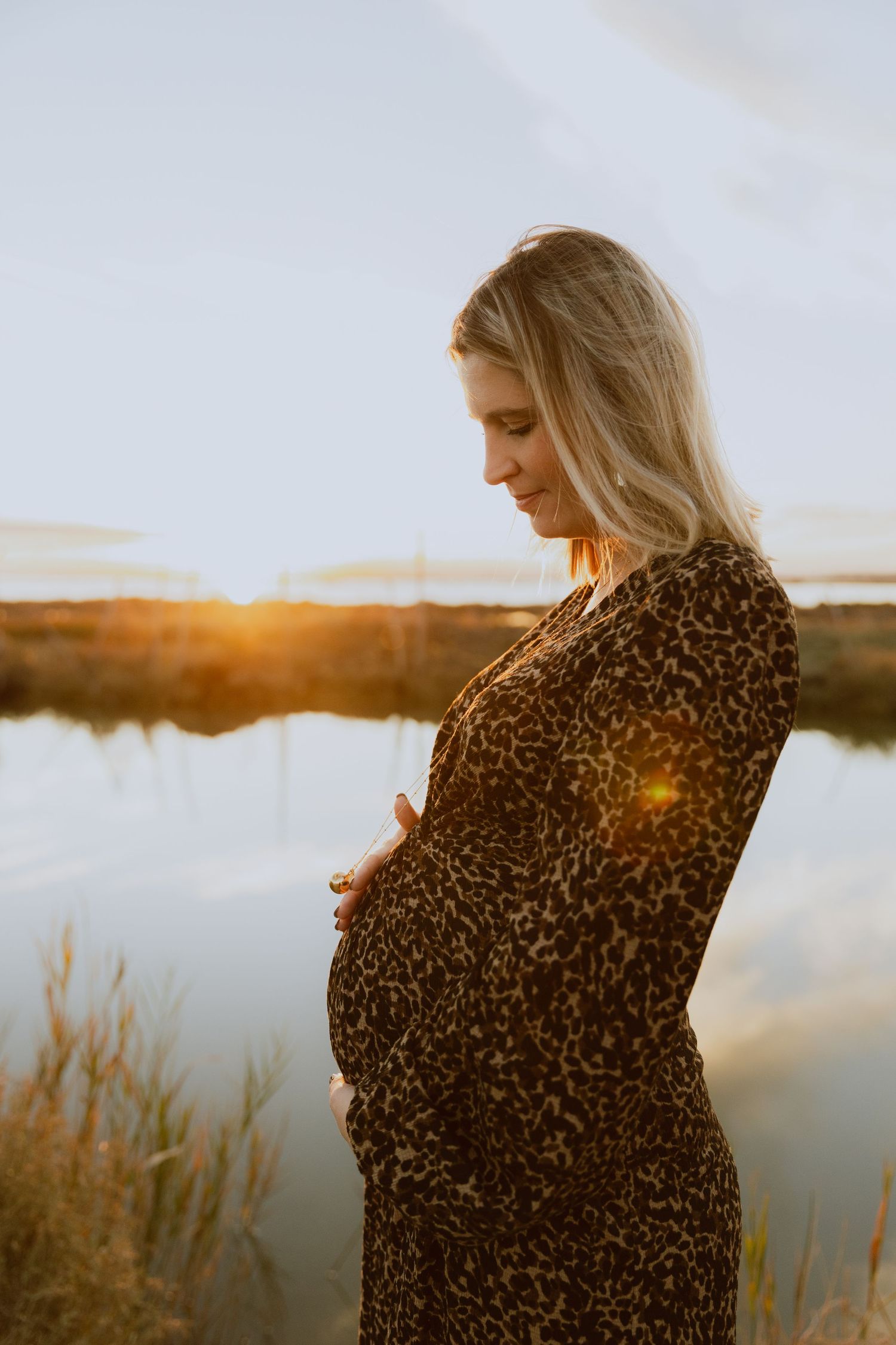 Femme enceinte regarde avec amour son ventre au coucher de soleil aux étangs de Mauguio pendant une séance photo de grossesse